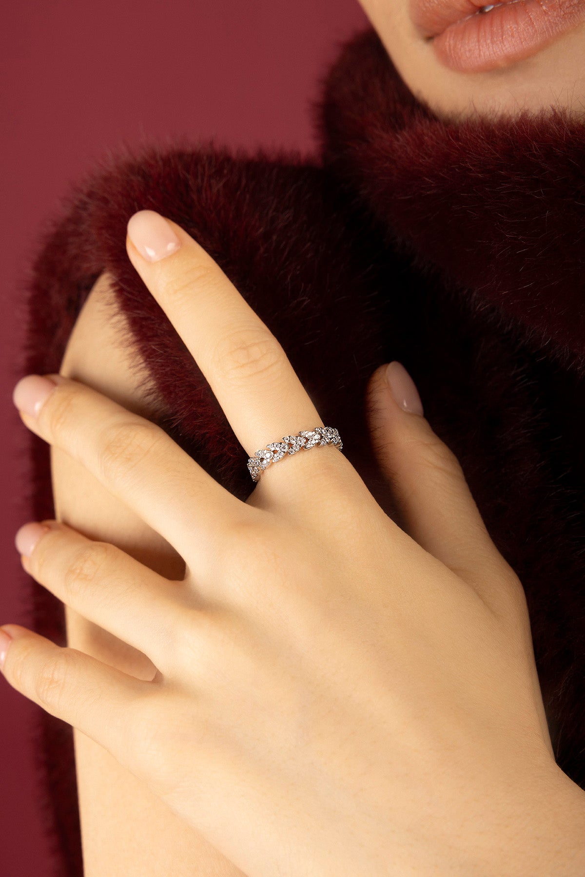 Woman wearing APM ring, éclat scintillant sur fourrure bordeaux, élégance intemporelle.