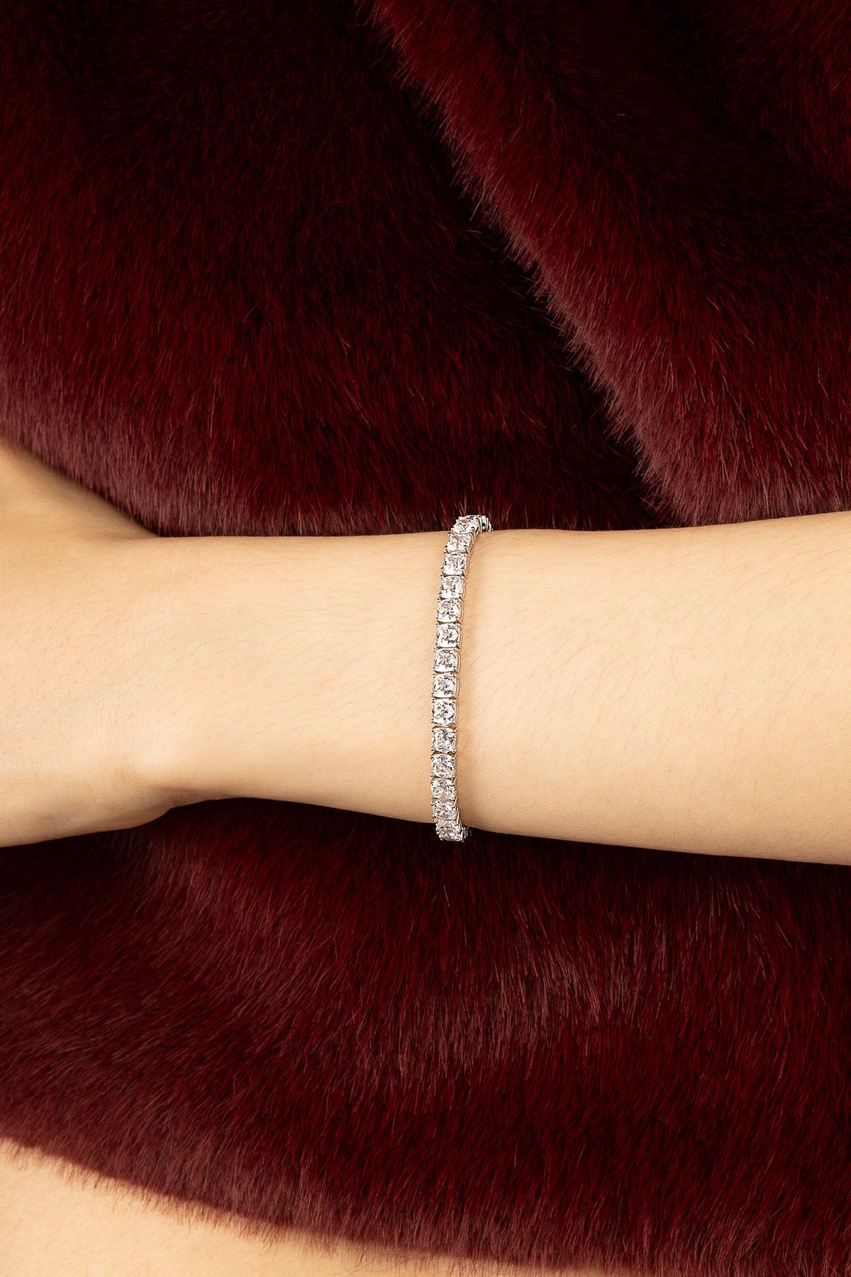 Femme portant le Bracelet Tennis APM Monaco, éclat scintillant sur fourrure bordeaux.