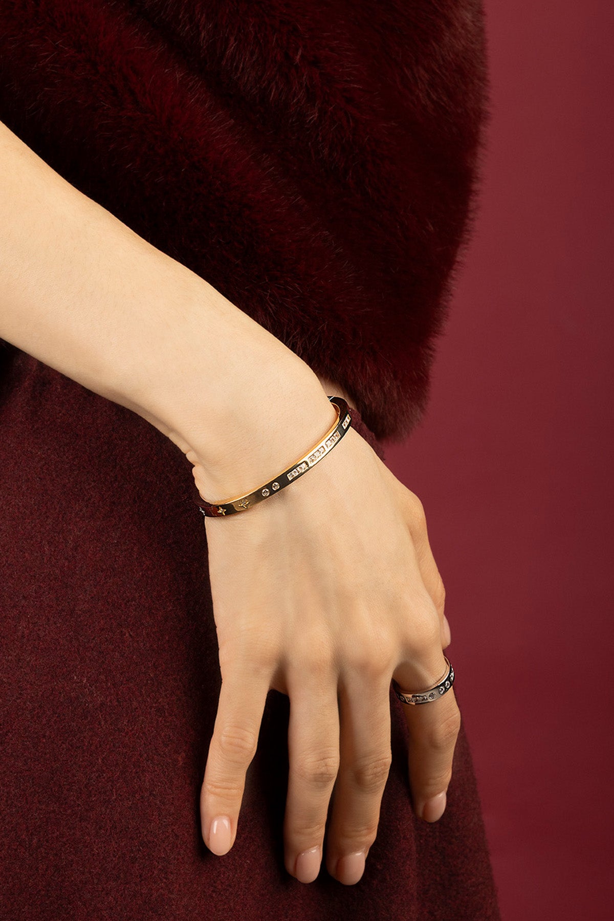 Femme portant le bracelet jonc APM Monaco, éclat doré sur velours bordeaux.