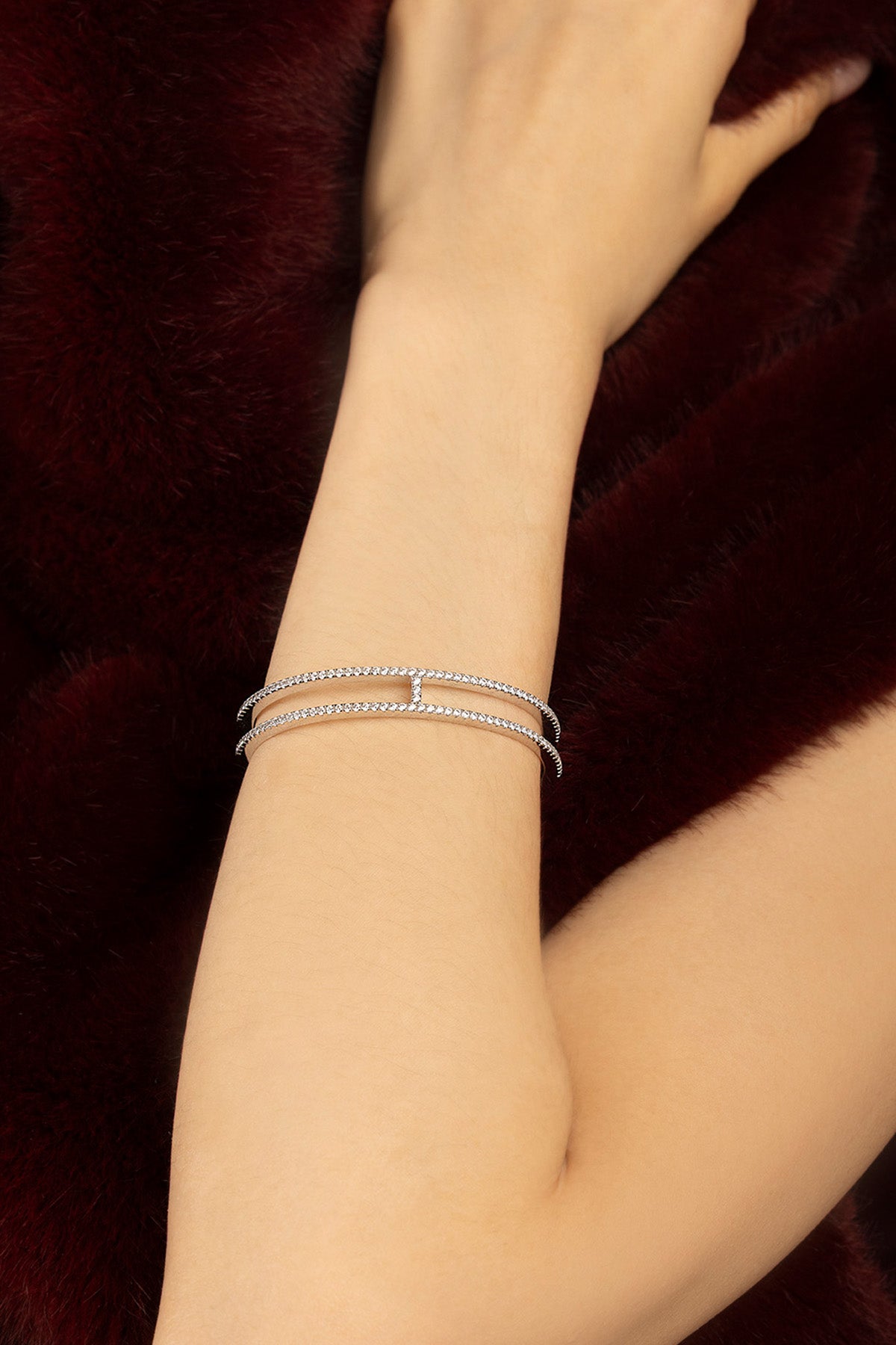 Femme portant le bracelet APM, double ligne scintillante, élégance moderne sur velours bordeaux.