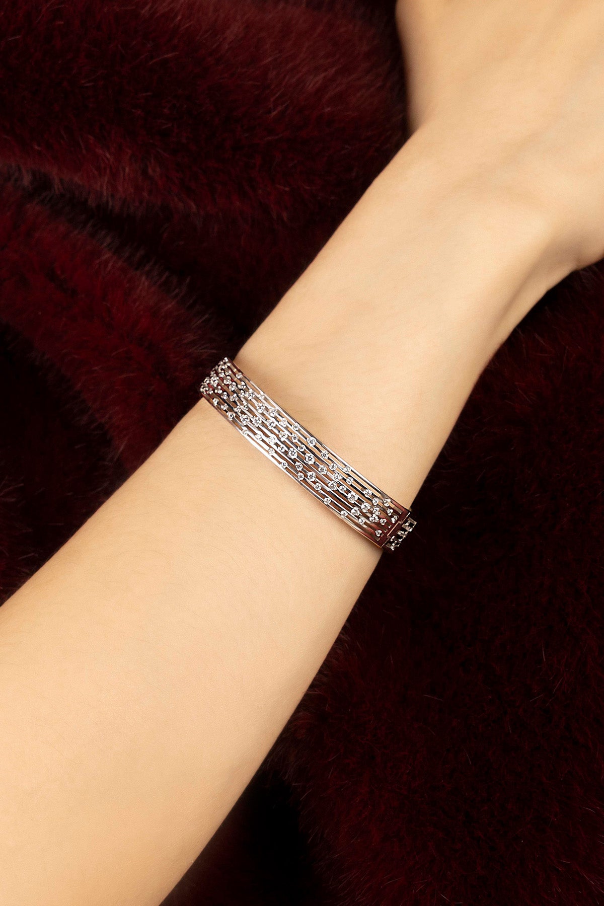 Woman wearing APM bracelet, éclat scintillant sur velours bordeaux.