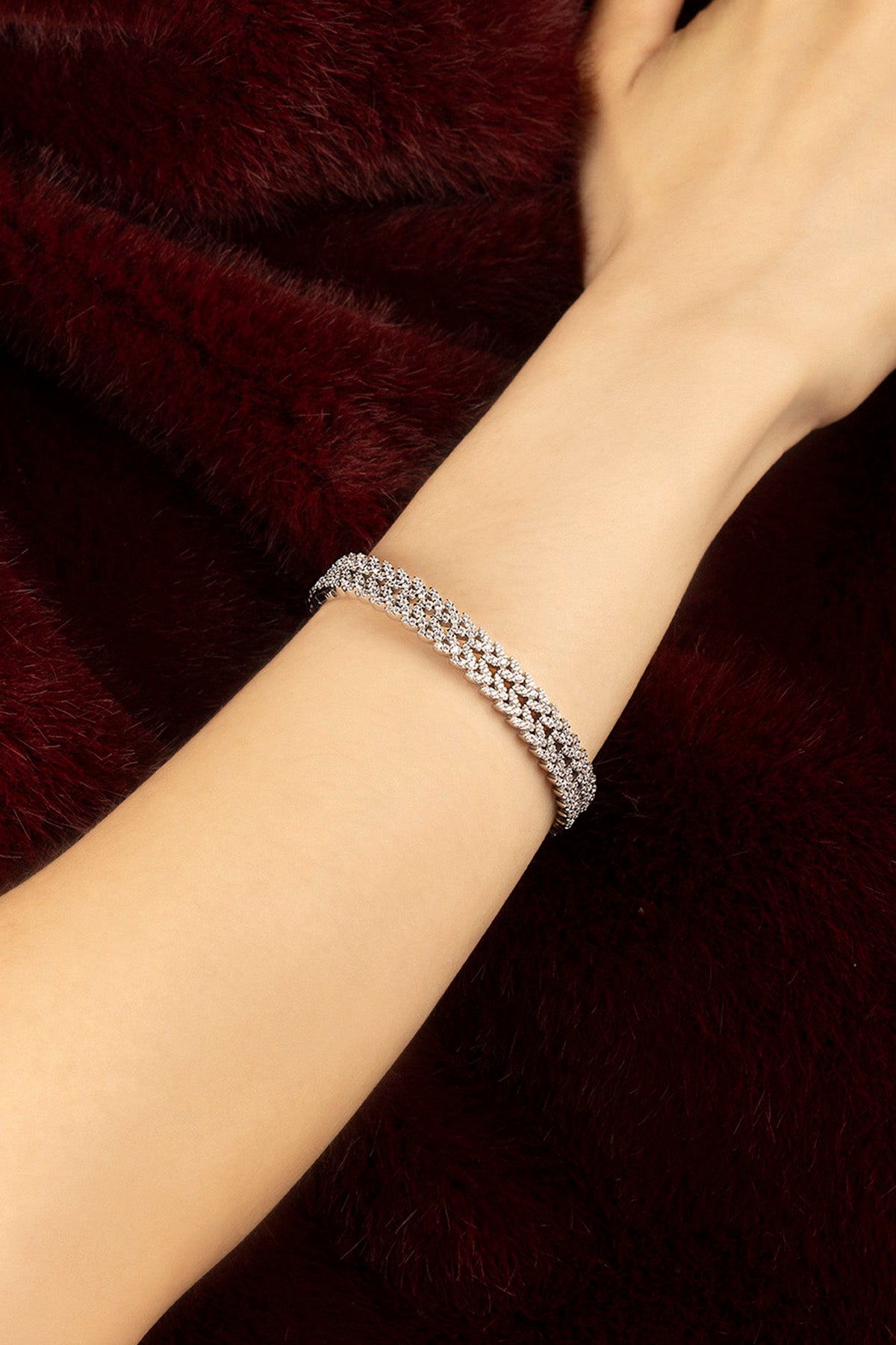 Femme portant le Bracelet APM, éclat scintillant sur fond bordeaux, élégance intemporelle.