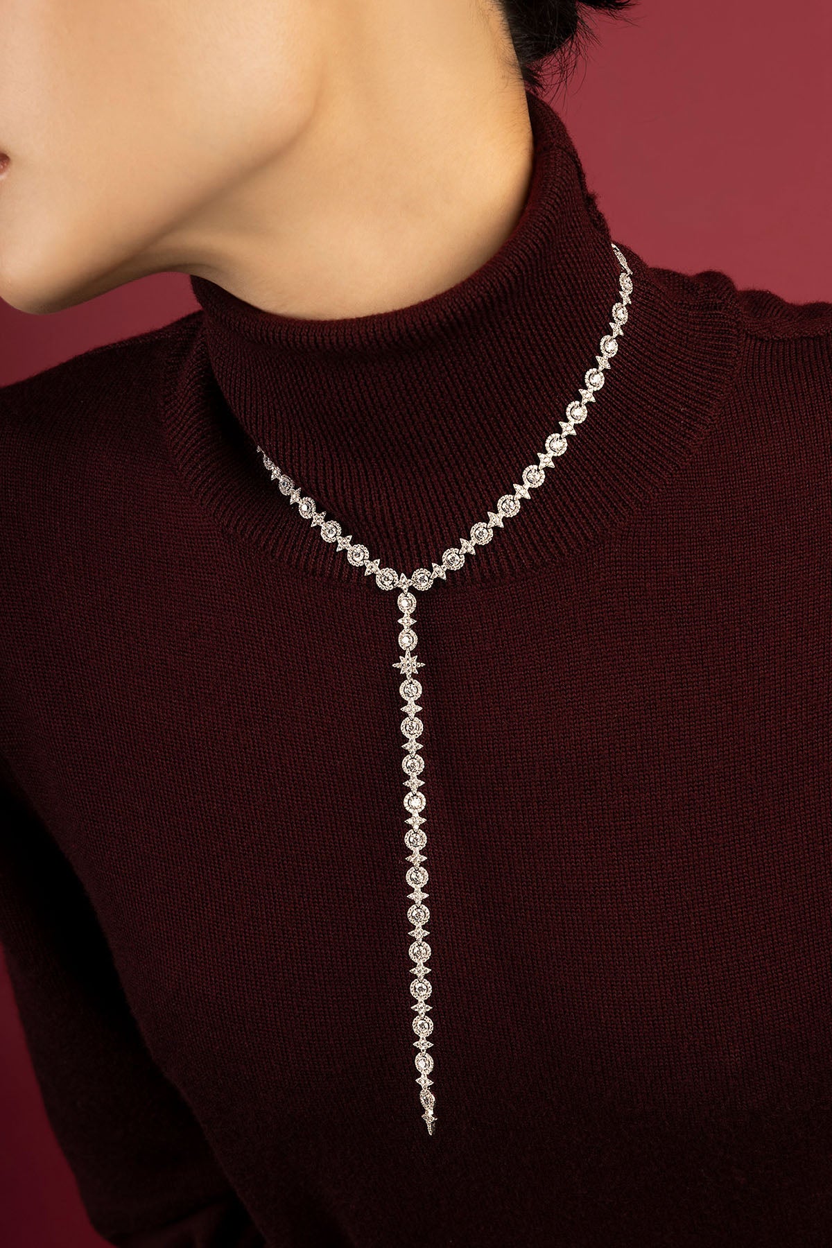 Femme portant un collier APM Monaco, cascade lumineuse sur bordeaux, élégance intemporelle.