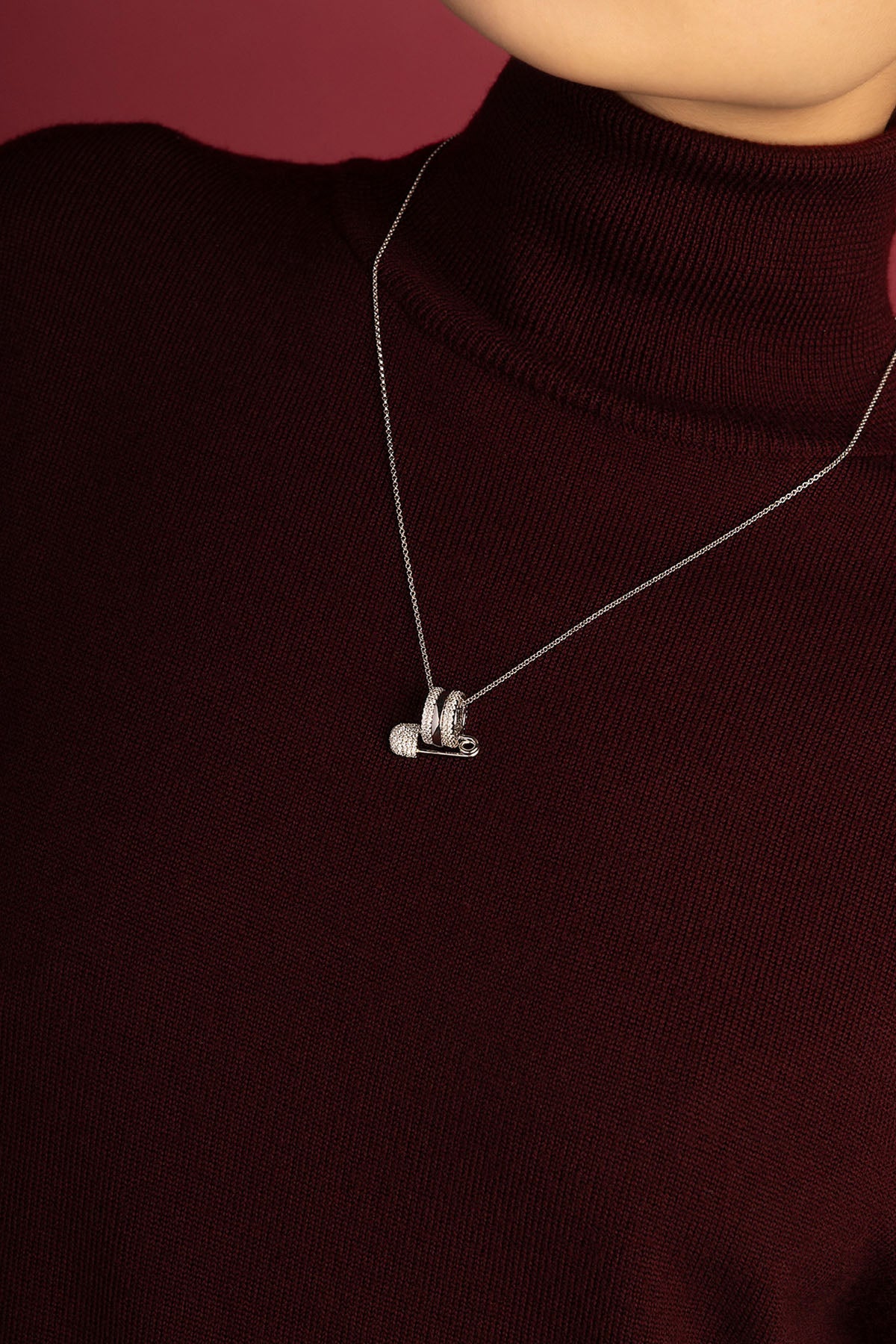 Femme portant le collier APM, une épingle scintillante posée sur un bordeaux profond.