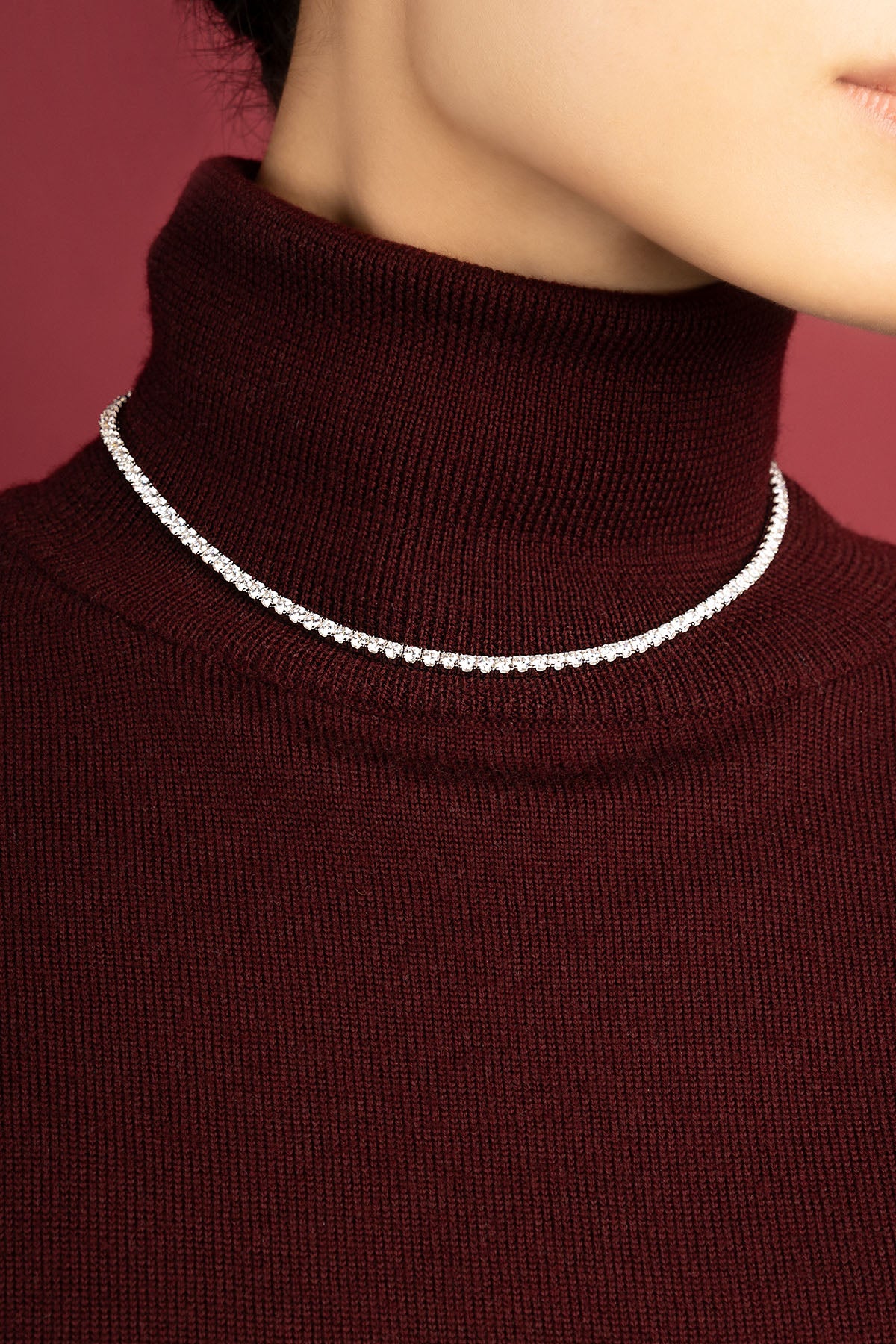 Femme portant le collier tennis APM Monaco, éclat scintillant sur col bordeaux.