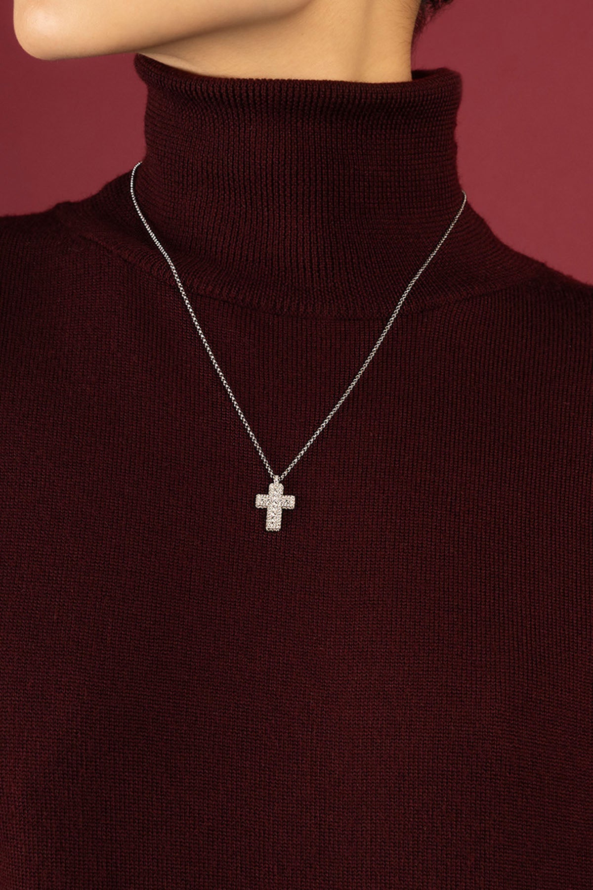 Femme portant le collier croix APM, une élégance délicate sur col bordeaux.