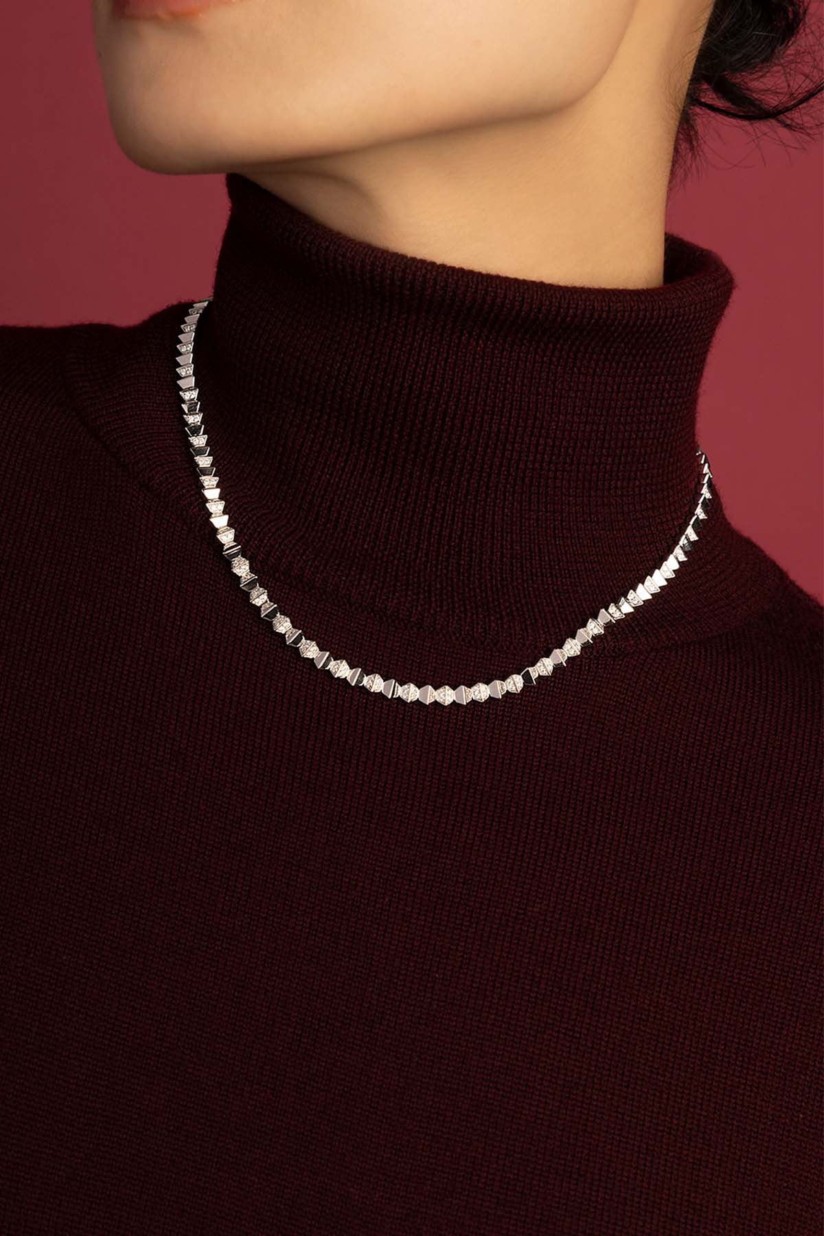 Femme portant le collier APM, éclat rhodié sur col roulé bordeaux, allure moderne et raffinée.