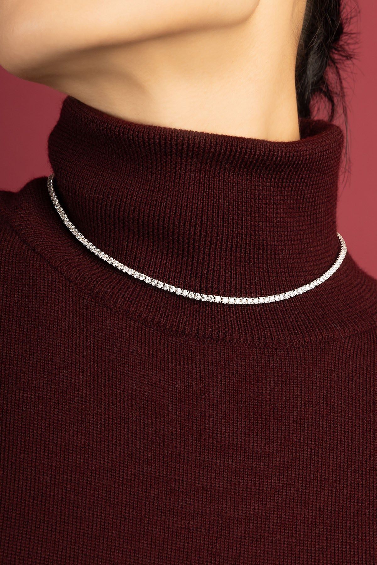 Femme portant le collier APM, éclat scintillant sur un col bordeaux, élégance intemporelle.