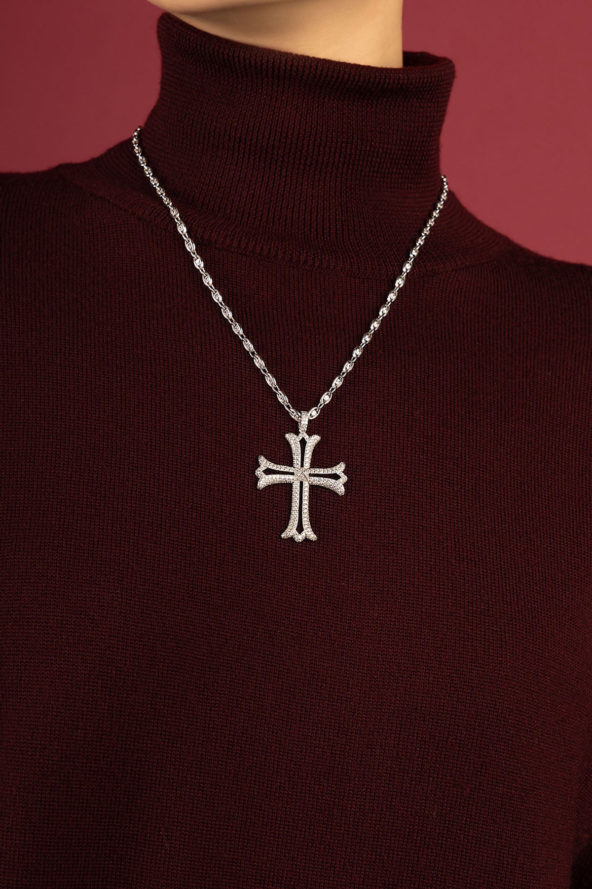 Femme portant le collier APM, une croix scintillante posée sur un col roulé bordeaux.