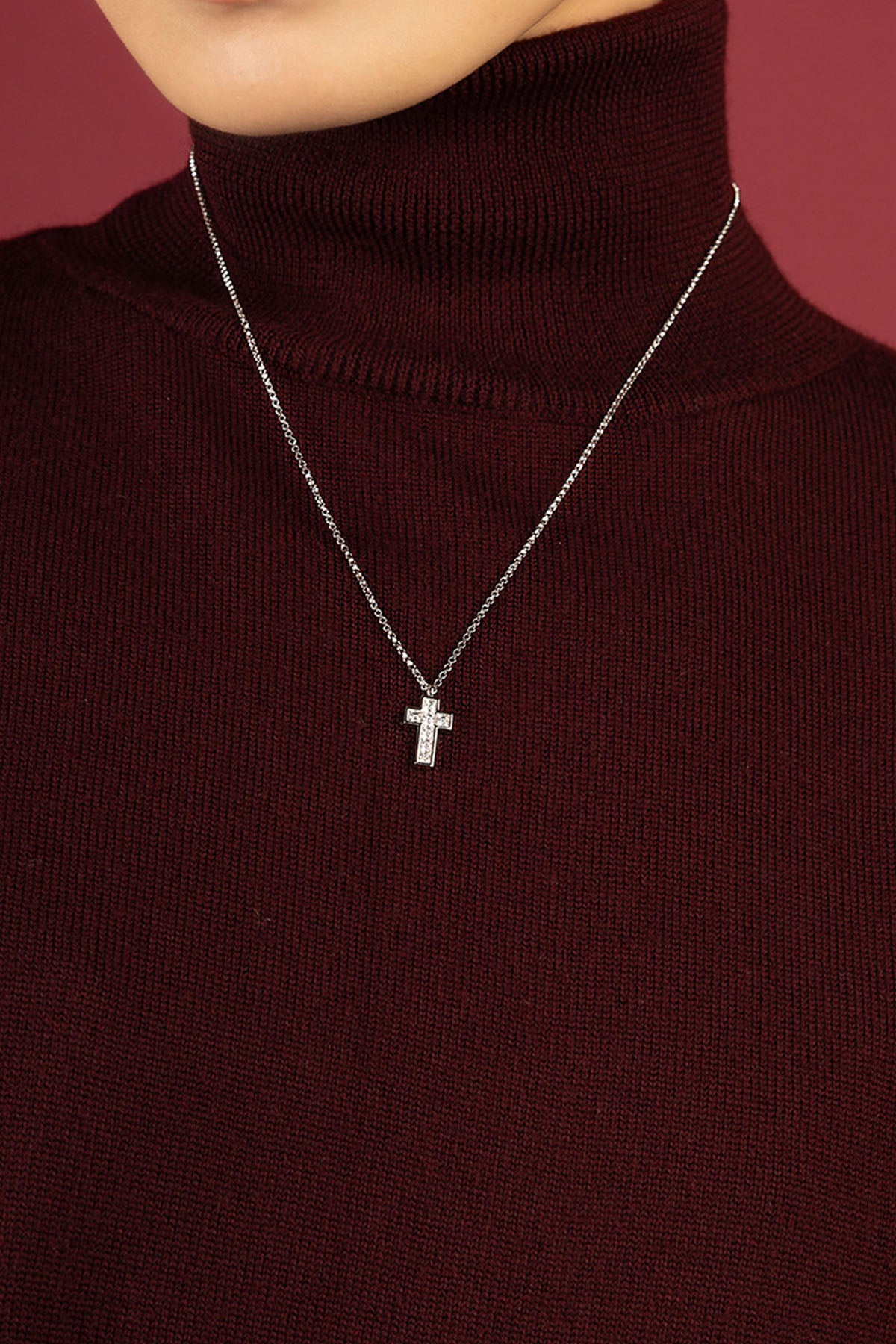 Femme portant le collier croix APM Monaco, éclat délicat sur un col bordeaux.