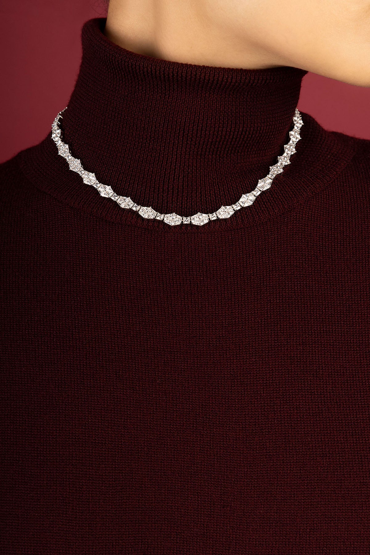 Femme portant un collier APM Monaco, éclat scintillant sur col bordeaux, élégance intemporelle.