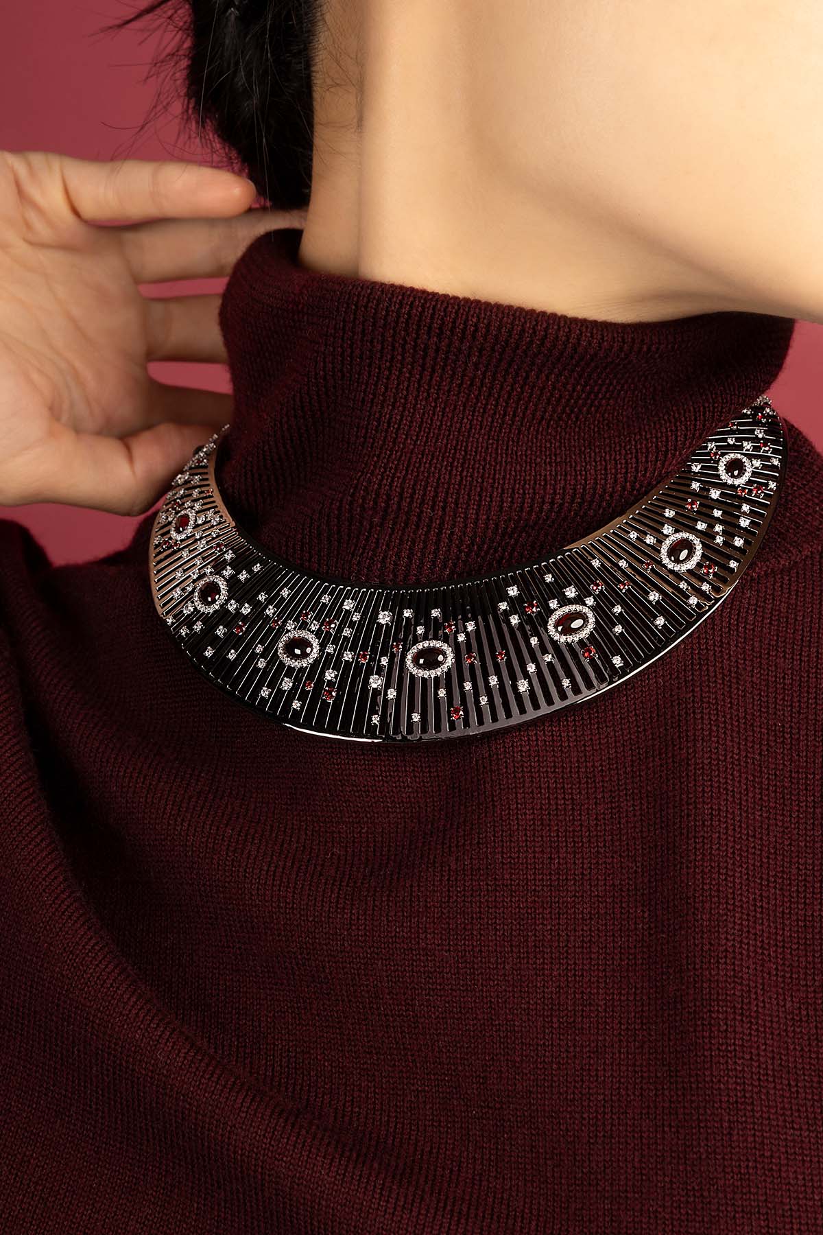 Femme portant le collier plastron APM Monaco, éclat mystérieux sur bordeaux profond.