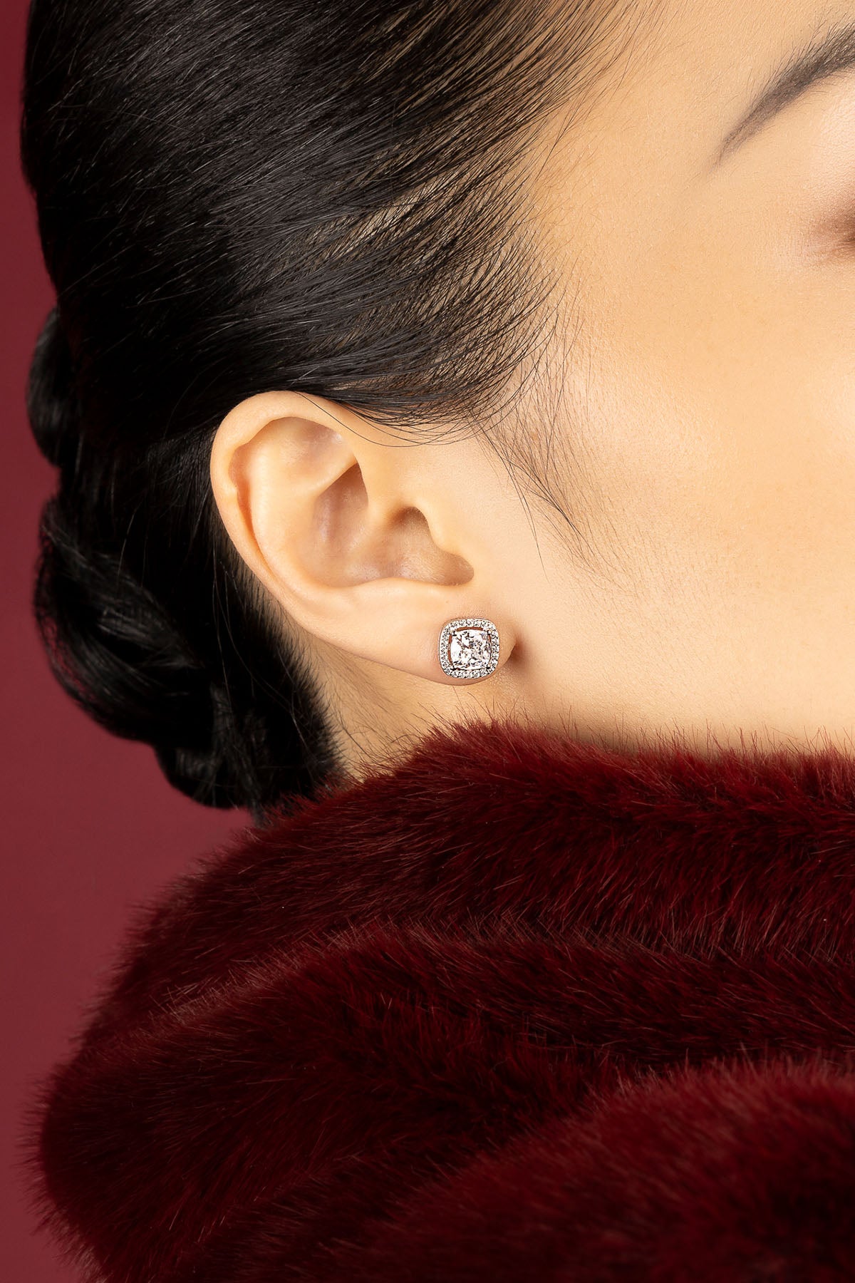 Femme portant les boucles d'oreilles APM, éclat précieux sur velours rouge profond.