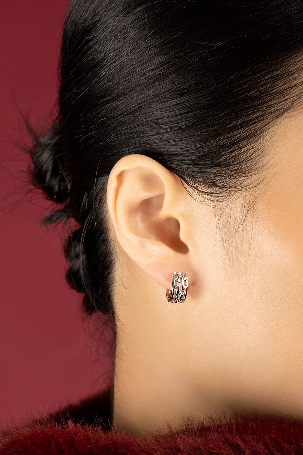 Femme portant les Boucles d'Oreilles APM, une allure raffinée sur fond bordeaux.