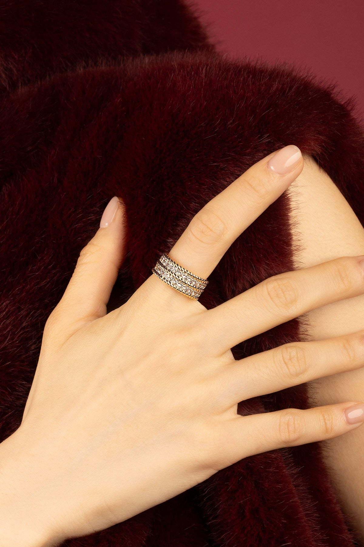Femme portant la bague APM, éclat doré sur velours bordeaux, élégance intemporelle.