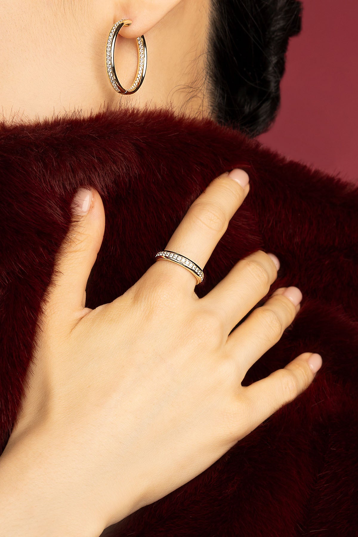 Femme portant les créoles et la bague APM Monaco, éclat doré sur fourrure bordeaux.