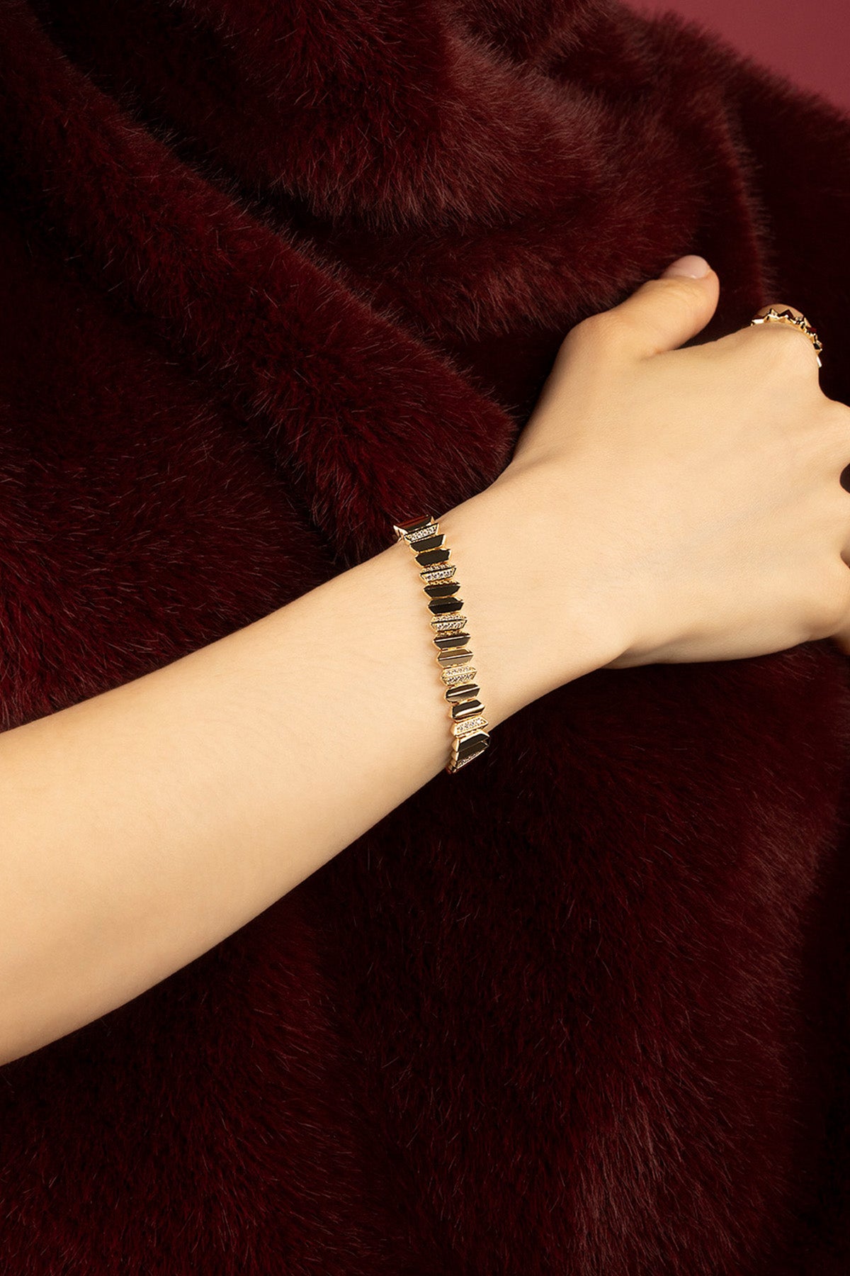 Femme portant le bracelet APM Monaco, éclat doré et noir sur fourrure bordeaux.