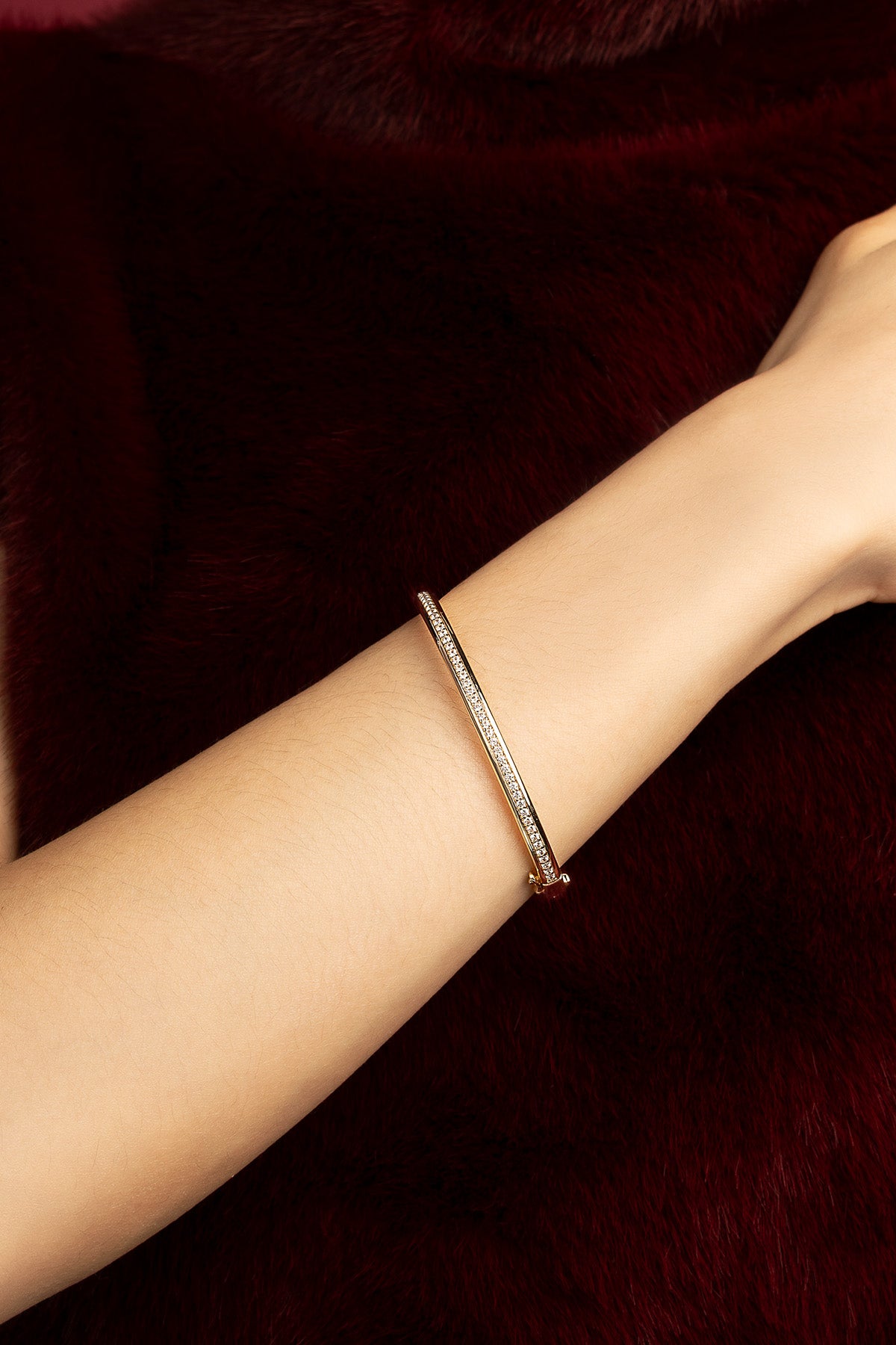 Femme portant le bracelet APM Monaco, éclat doré et allure raffinée sur velours grenat.