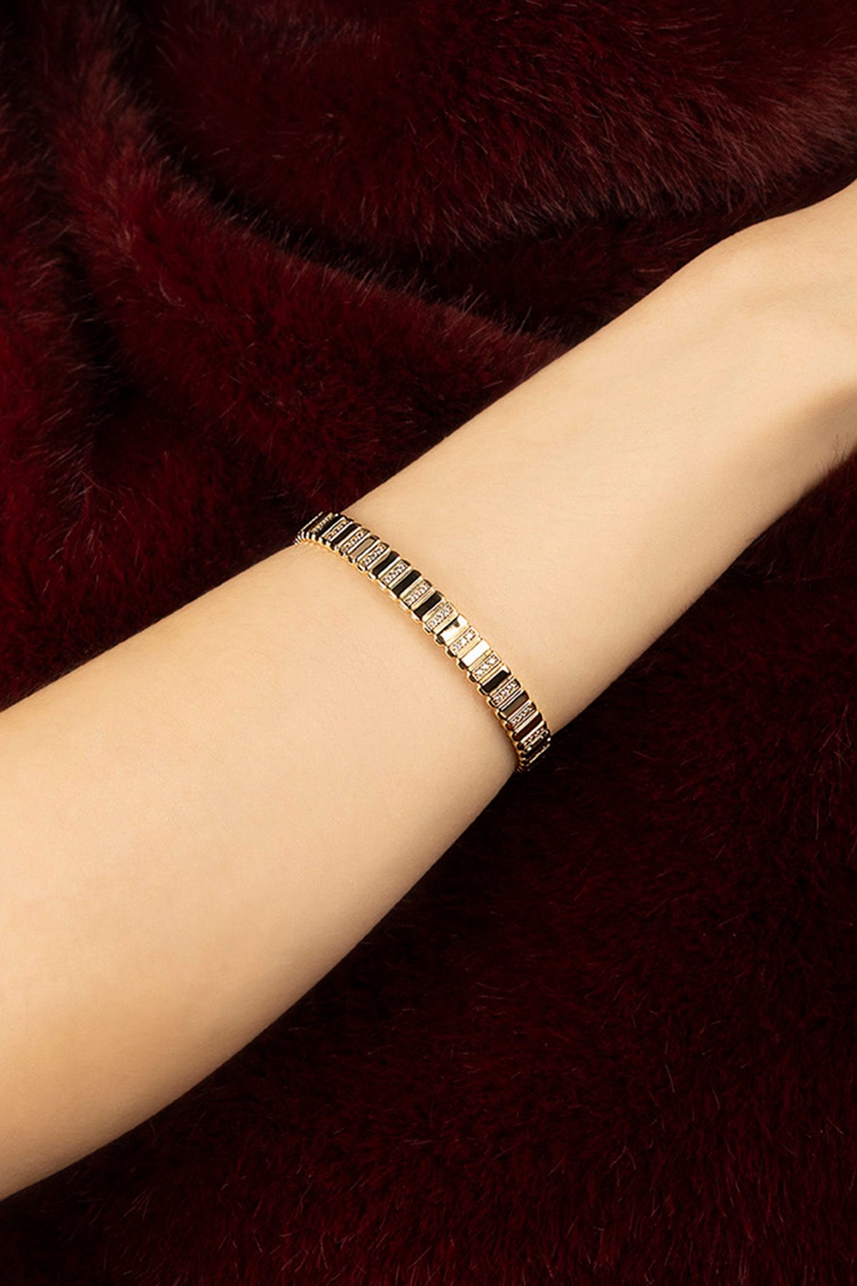 Femme portant le bracelet APM, éclat doré sur fourrure bordeaux, élégance feutrée.