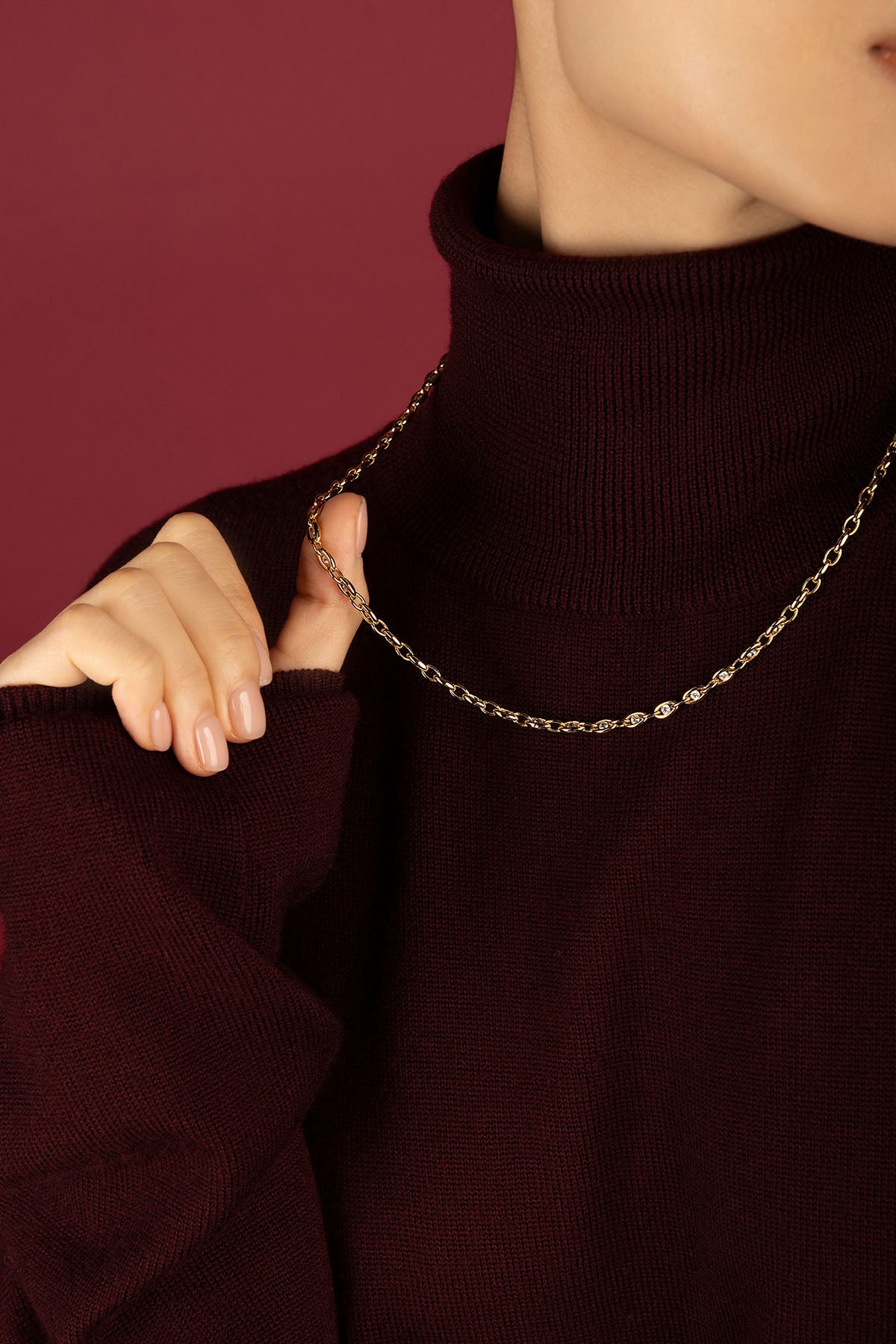 Femme portant un collier chaîne APM, éclat doré sur bordeaux, élégance intemporelle.