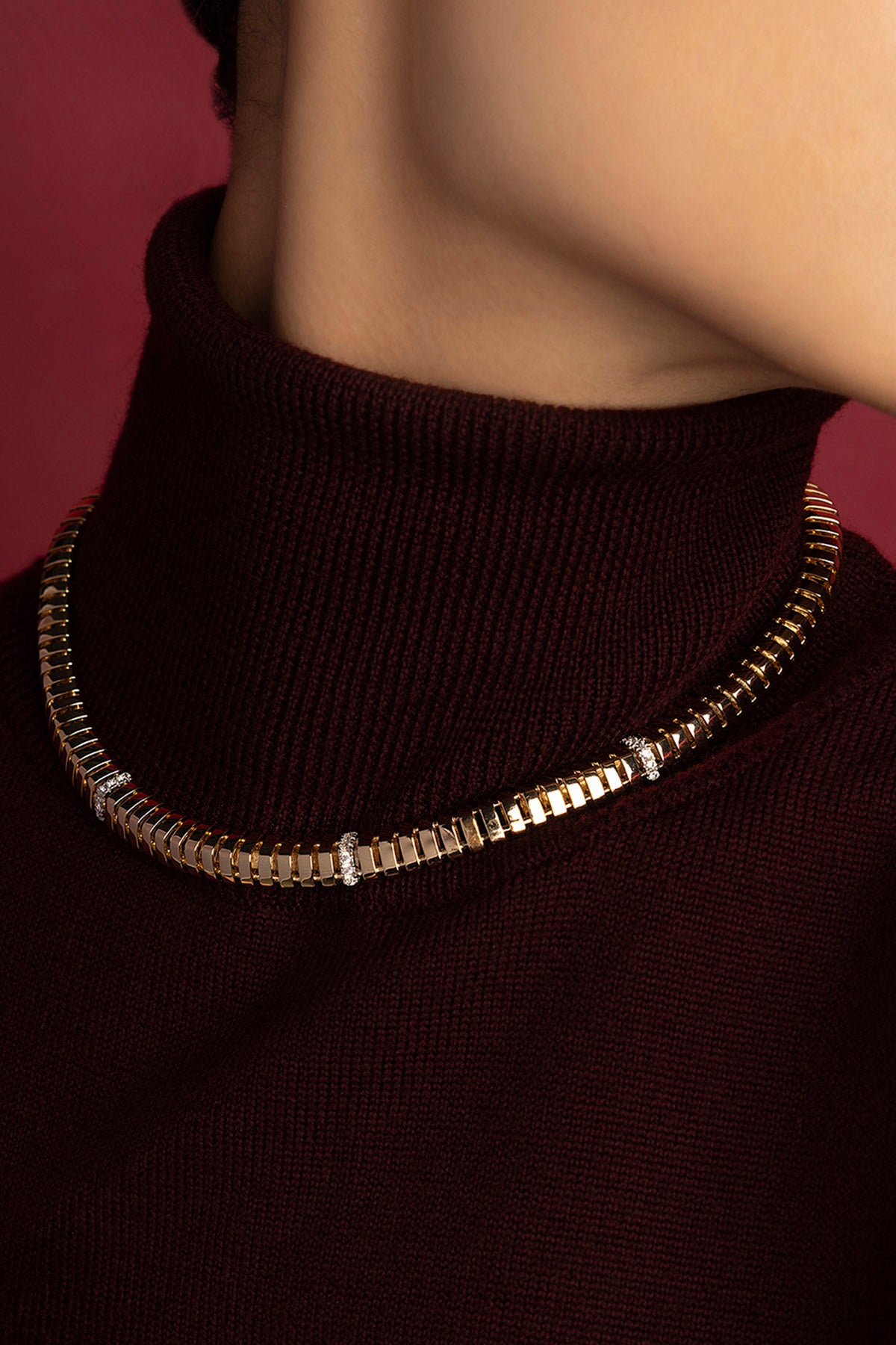 Femme portant un collier APM Monaco, éclat doré et allure sophistiquée sur maille bordeaux.