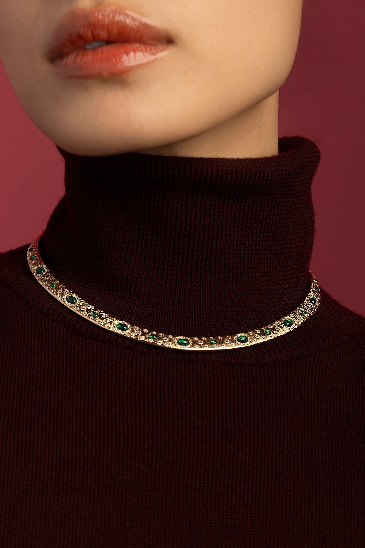 Femme portant le collier APM, éclats verts et allure précieuse sur col roulé bordeaux.