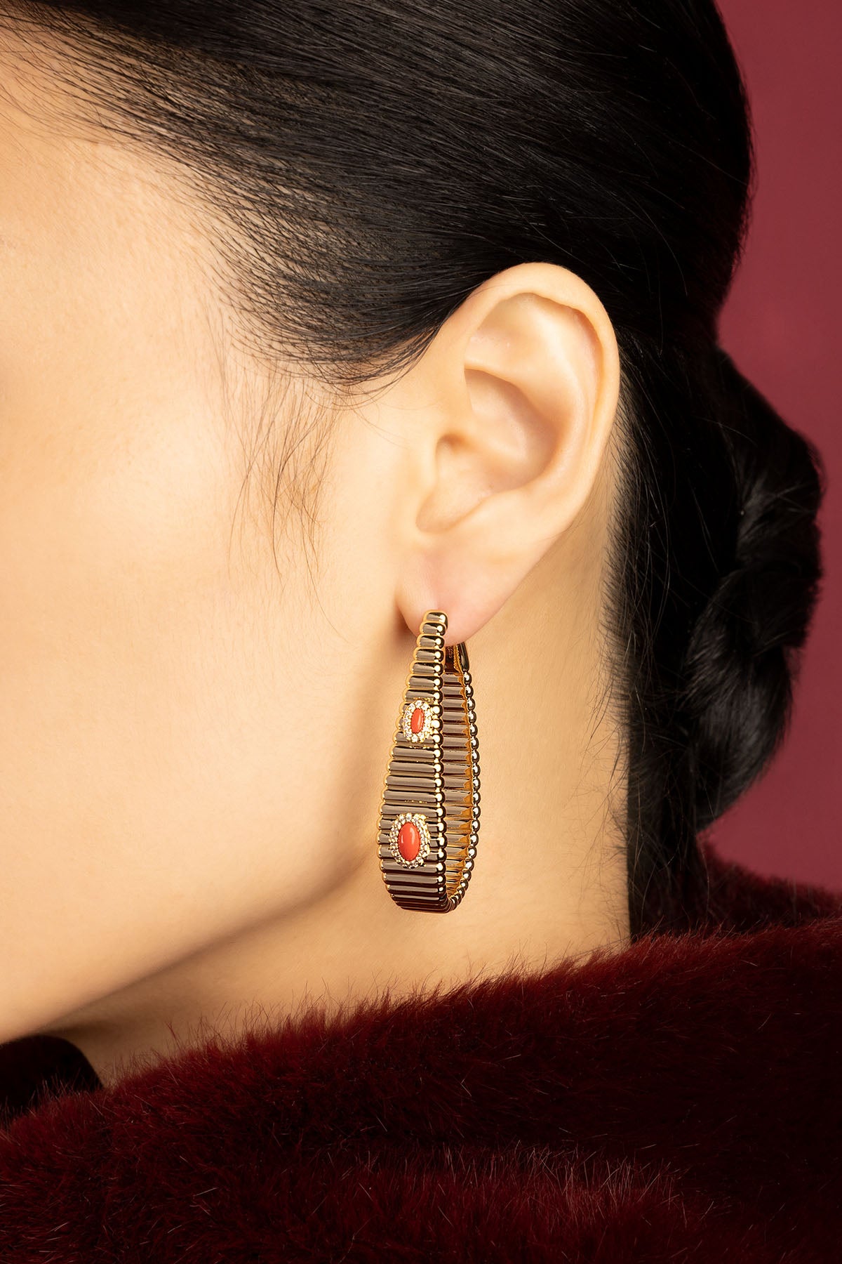 Femme portant les créoles APM, une allure sculpturale rehaussée de touches corail lumineuses.