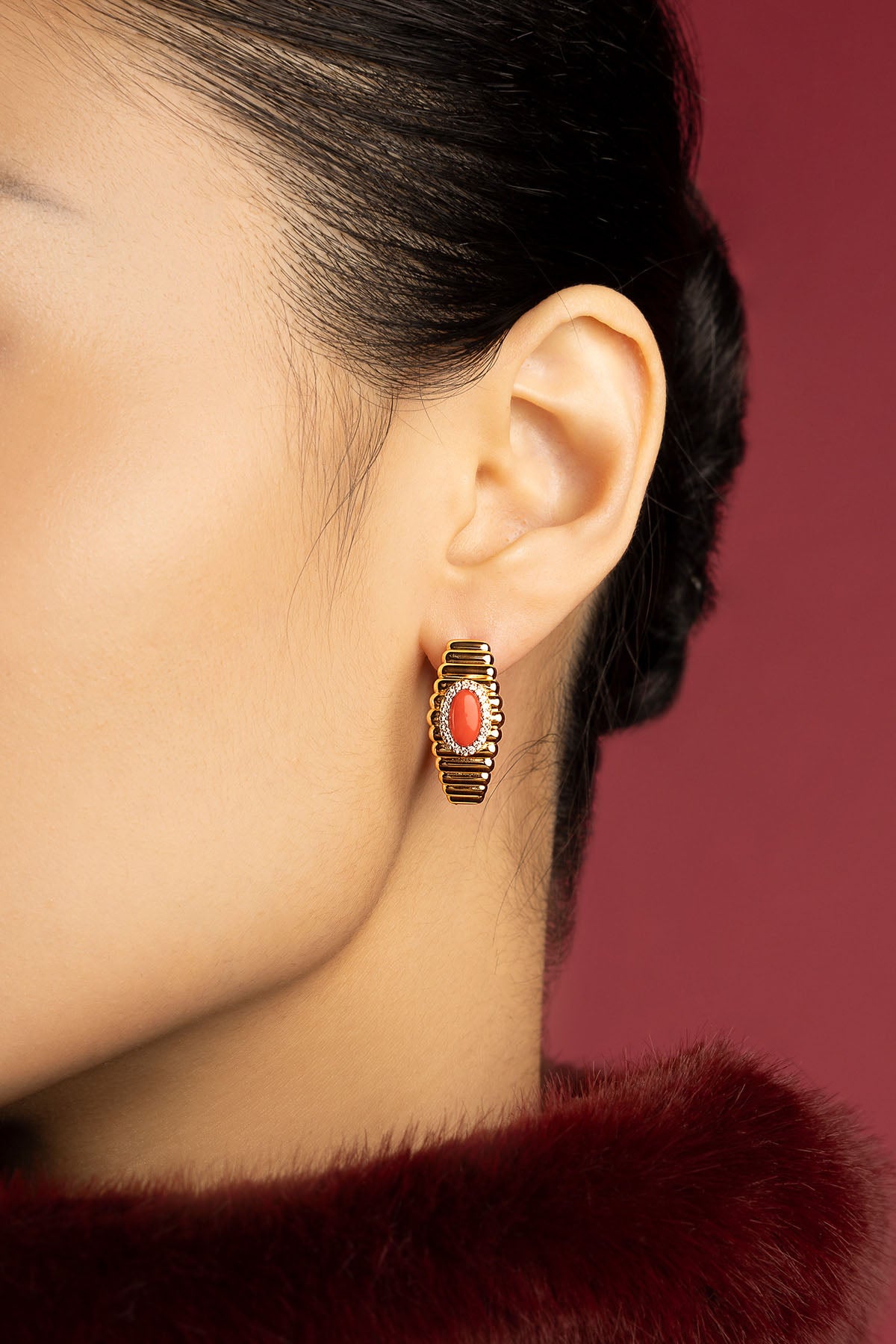 Femme portant les boucles d'oreilles APM, une touche corail pleine d'élégance intemporelle.
