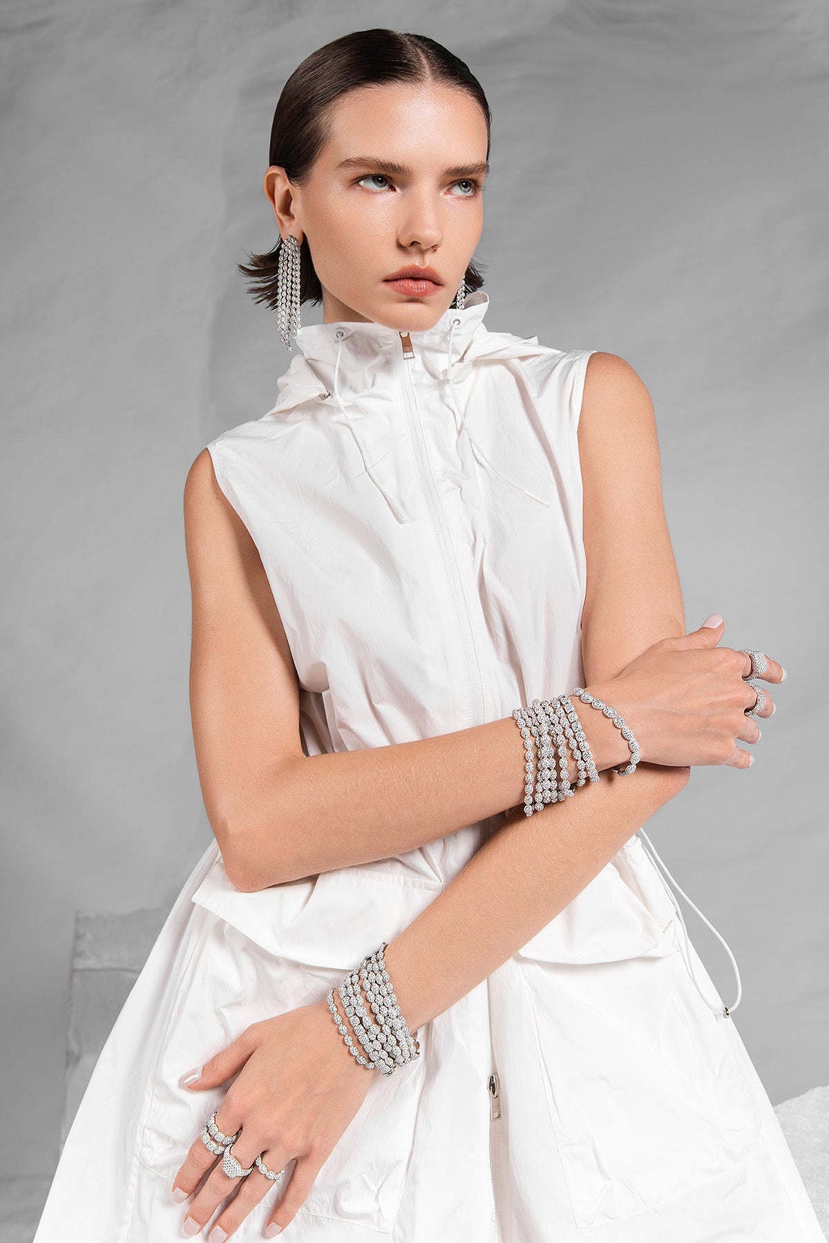 Model wearing a white sleeveless outfit with APM MONACO statement pave silver rings and bracelets on a gray background