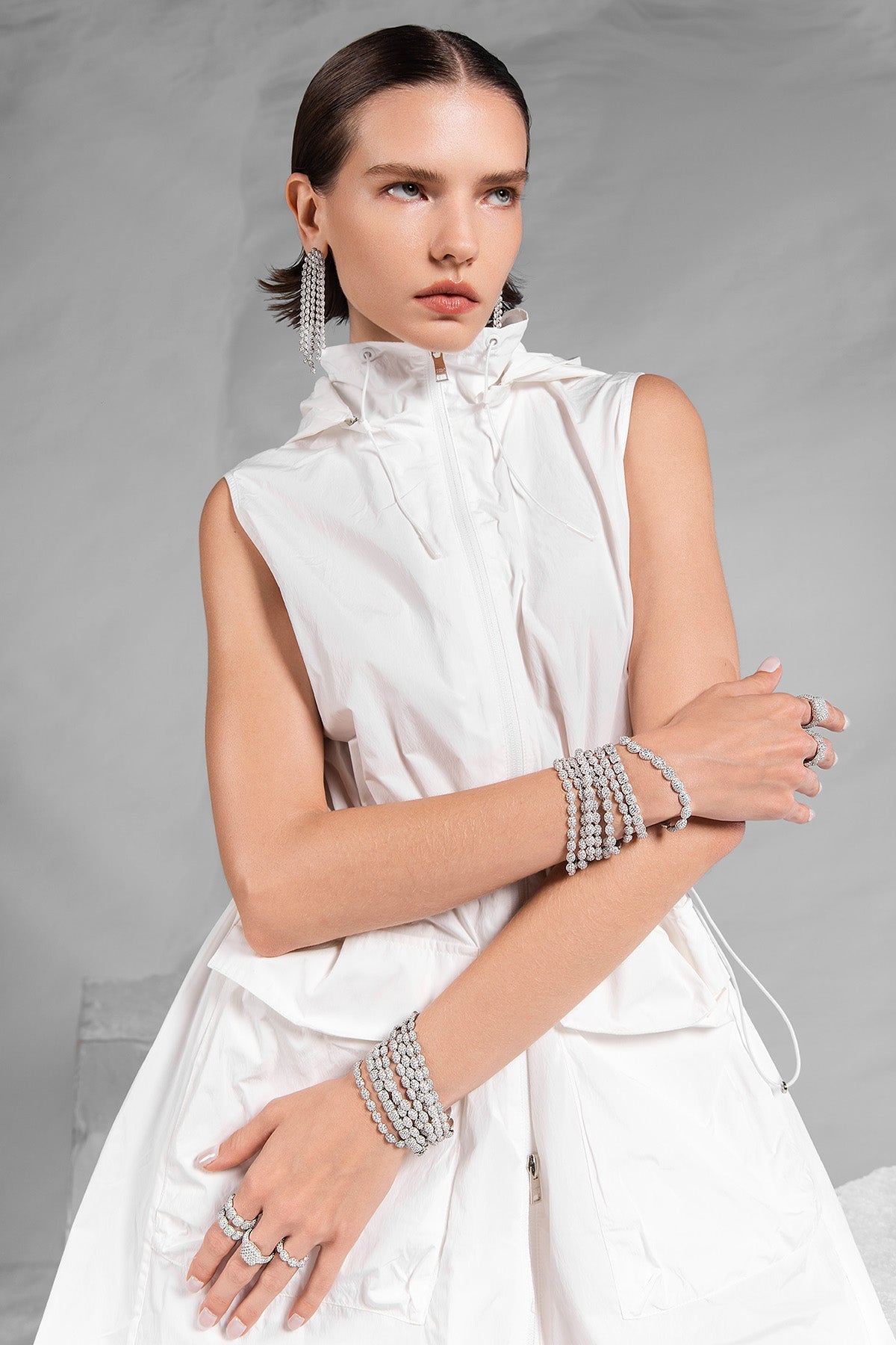 Woman wearing a white sleeveless dress with APM MONACO pave jewelry in silver on a gray background