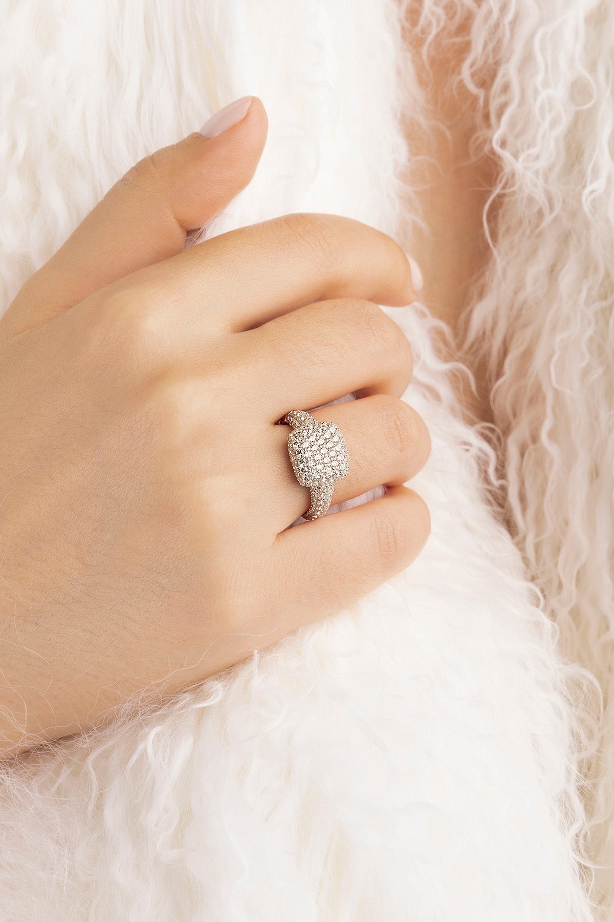 Hand wearing a APM MONACO pave silver ring with white stones on a soft, light-colored background