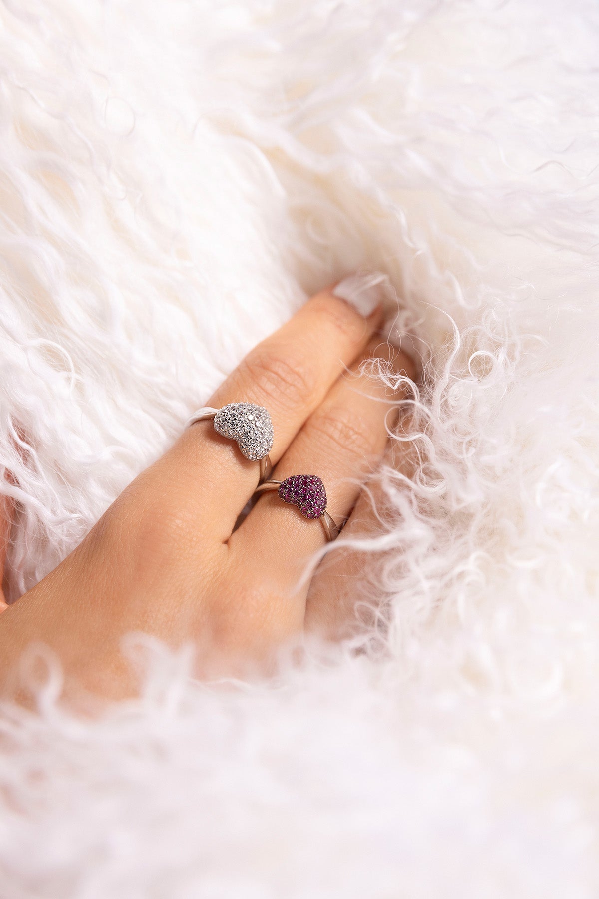 Hand wearing two heart-shaped APM MONACO rings in silver on a fluffy white surface