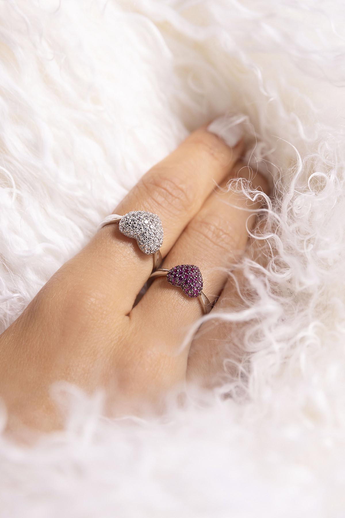 APM MONACO heart-shaped rings in silver on finger against a soft white background