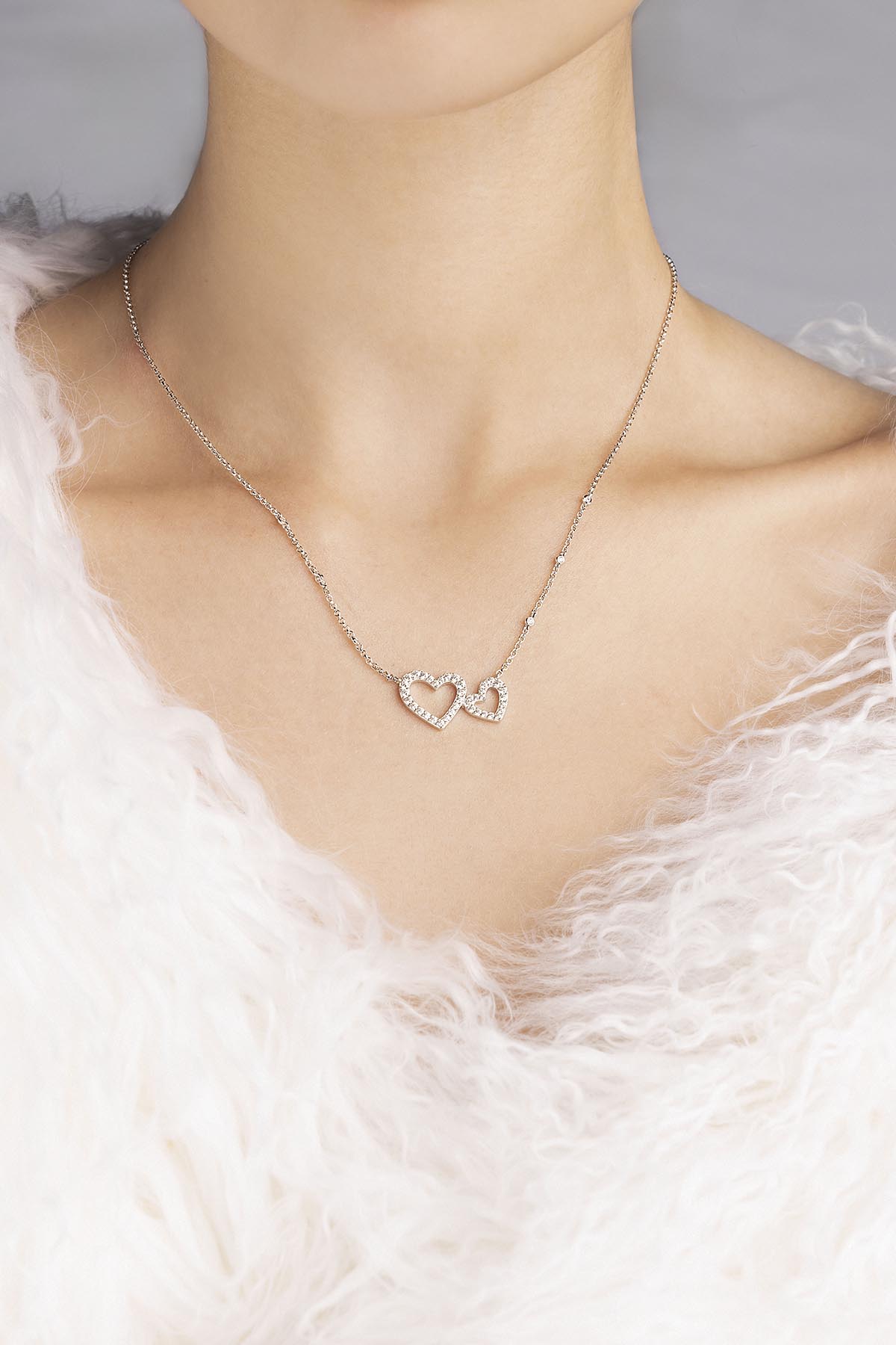 Necklace with a heart-shaped pendant from APM MONACO on a person and wearing a white feathered garment.
