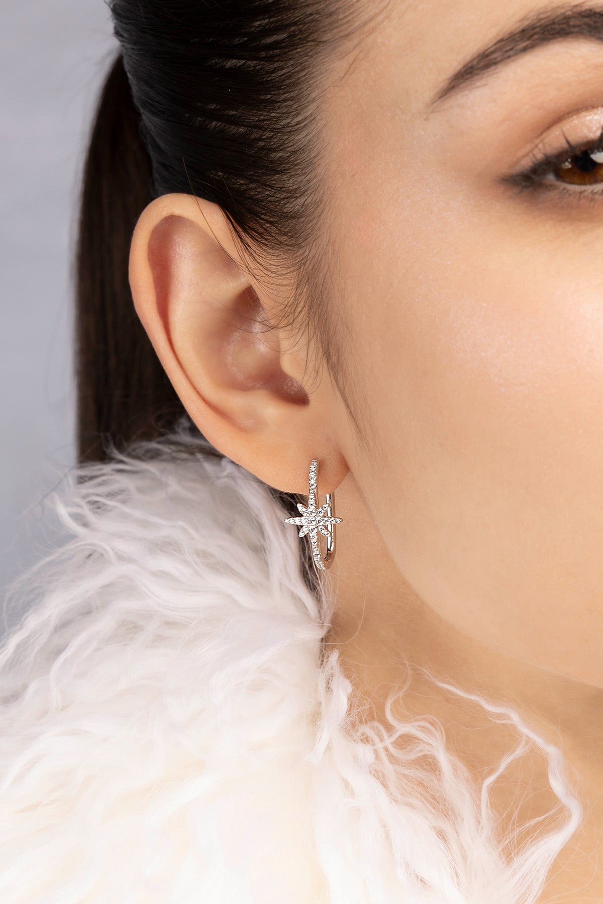 Close-up of a woman wearing a silver earring with a white feathered garment.