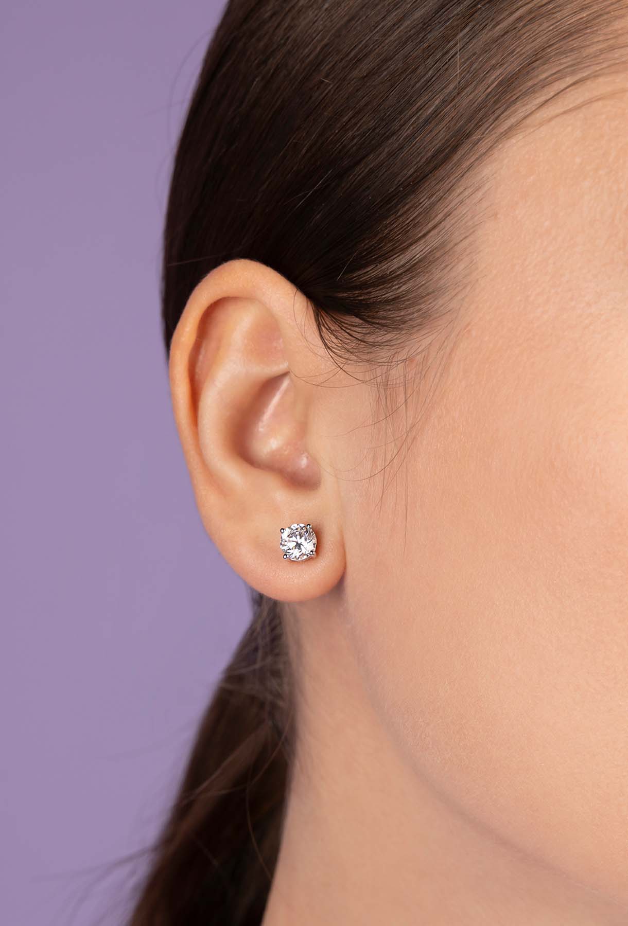 Closeup of an ear wearing a diamond earring against a purple background