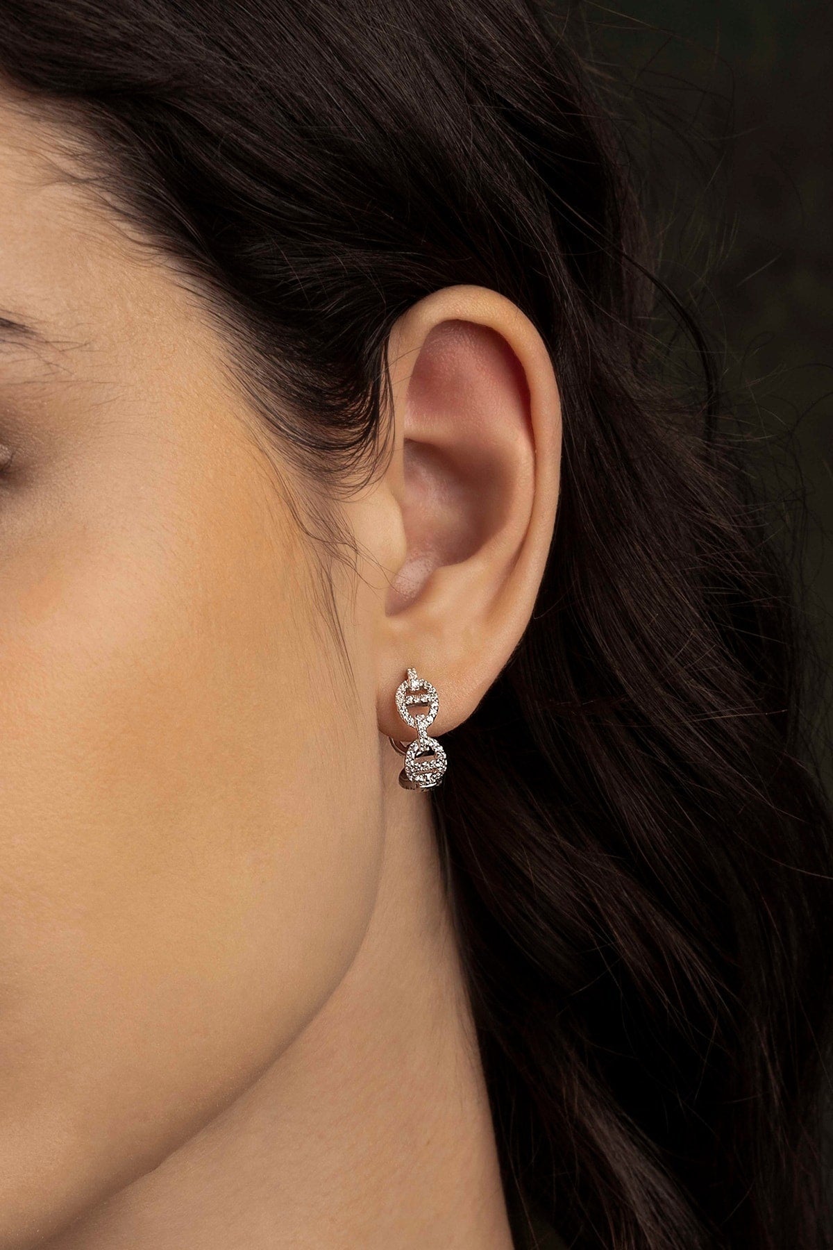 Close-up of an ear wearing a diamond earring with dark hair and skin background