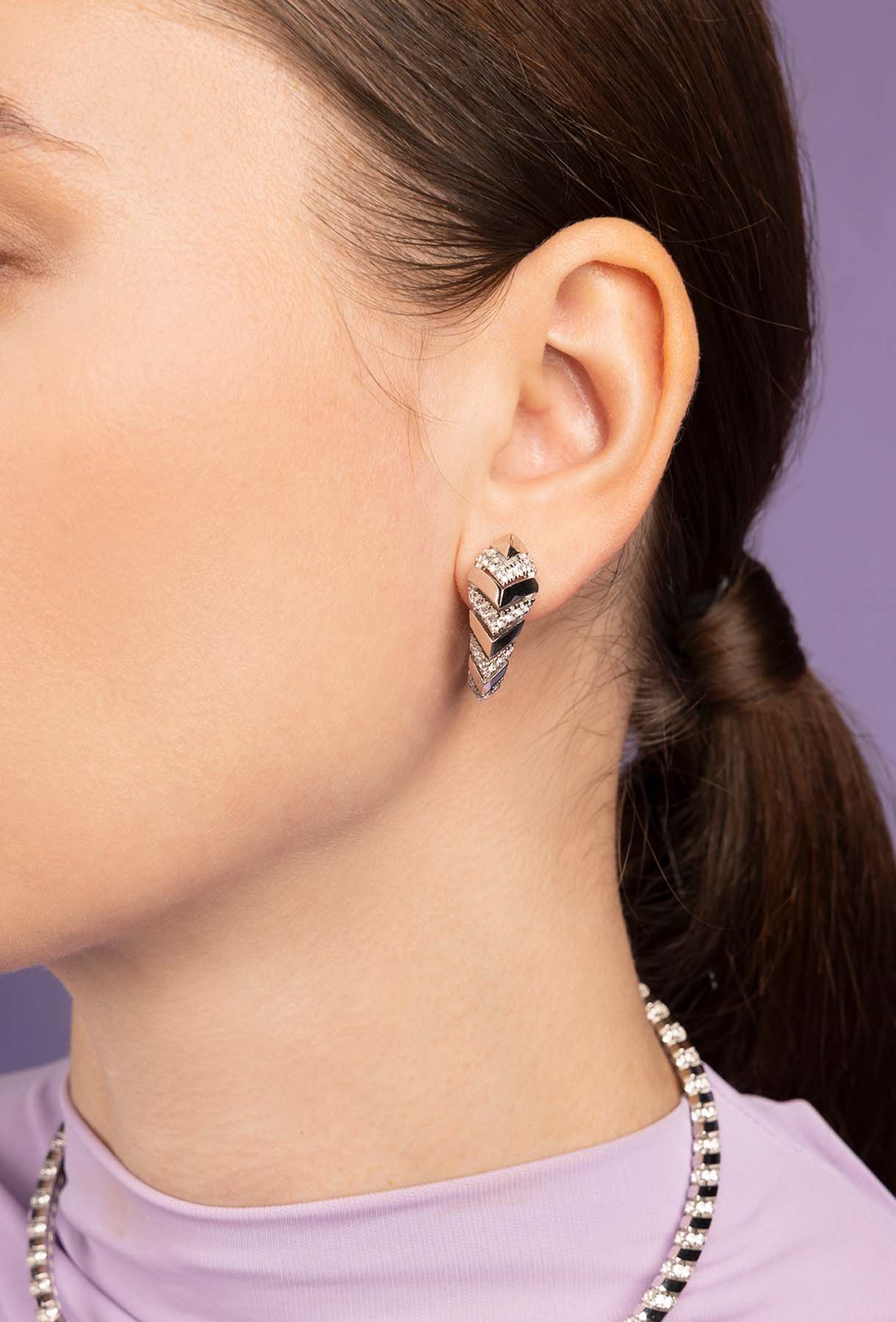 Closeup of a person wearing APM MONACO KAA silver earrings with a purple background