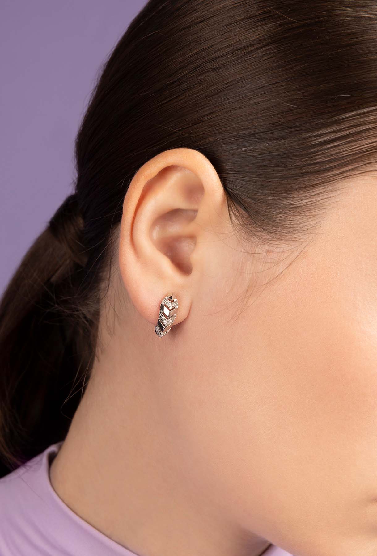 Closeup of a person wearing APM MONACO silver earring with a black design on a light purple background