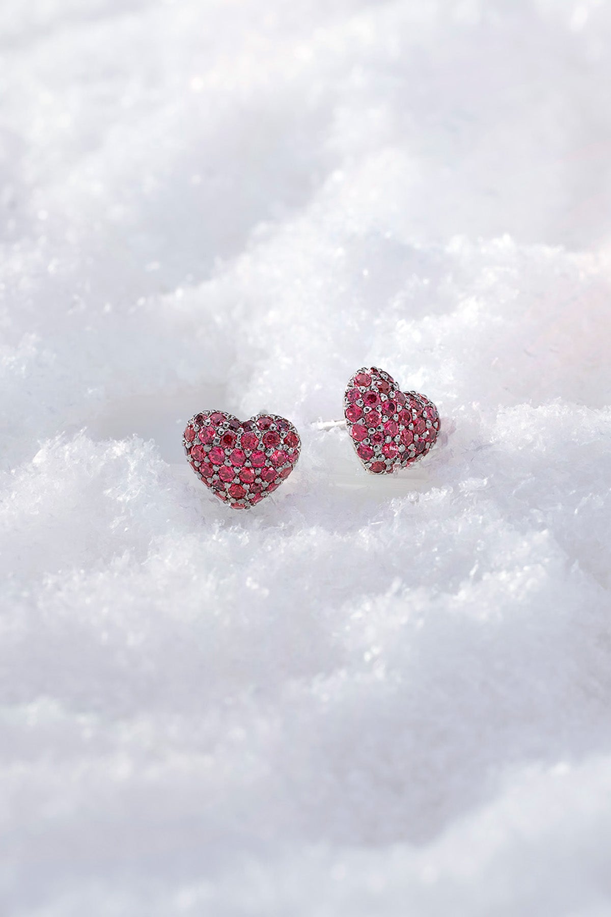 APM MONACO heart-shaped earrings with fuchsia stones on a white snowy background