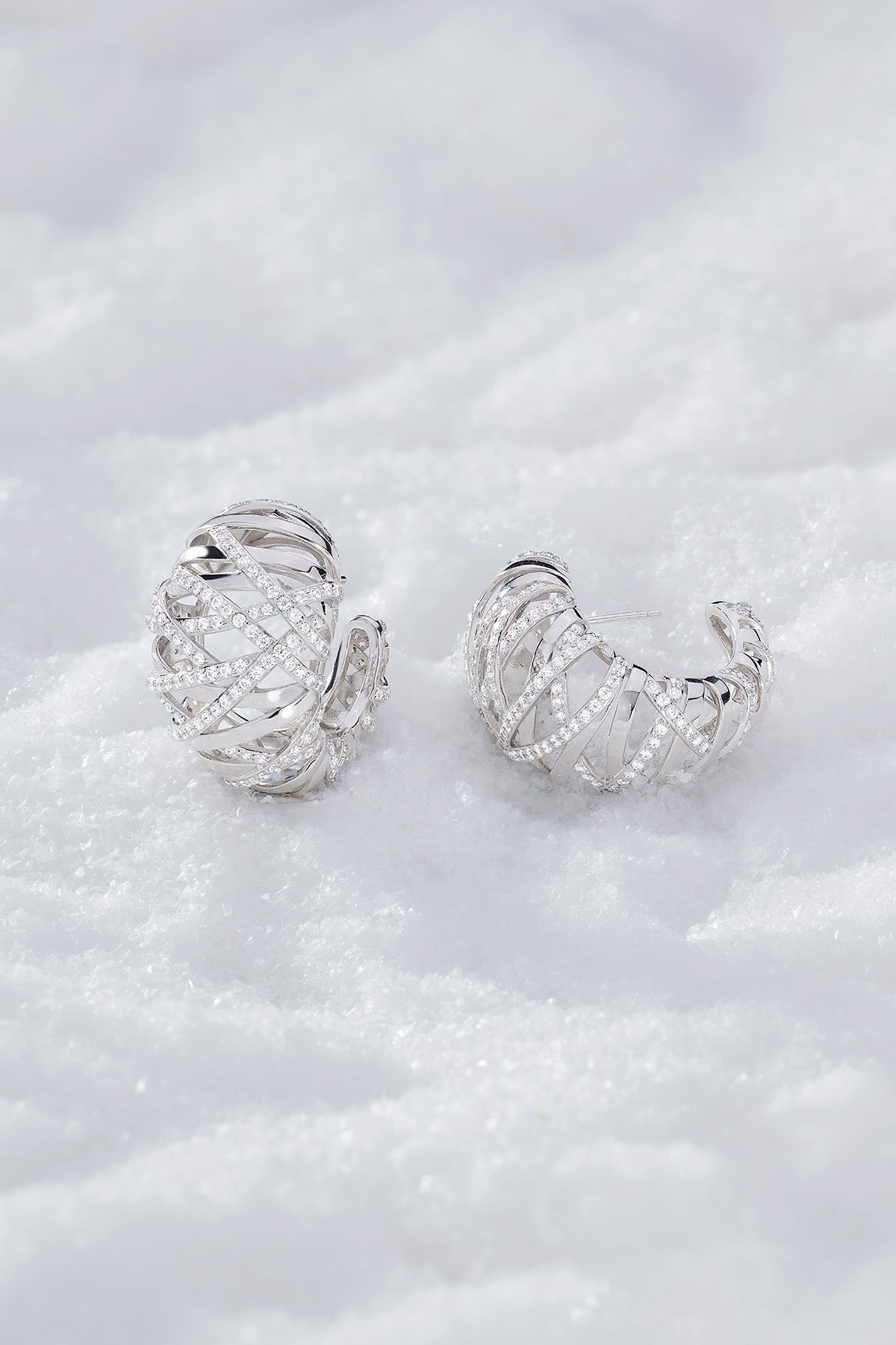 Pair of APM MONACO enlace hoop earrings in silver on a textured white surface