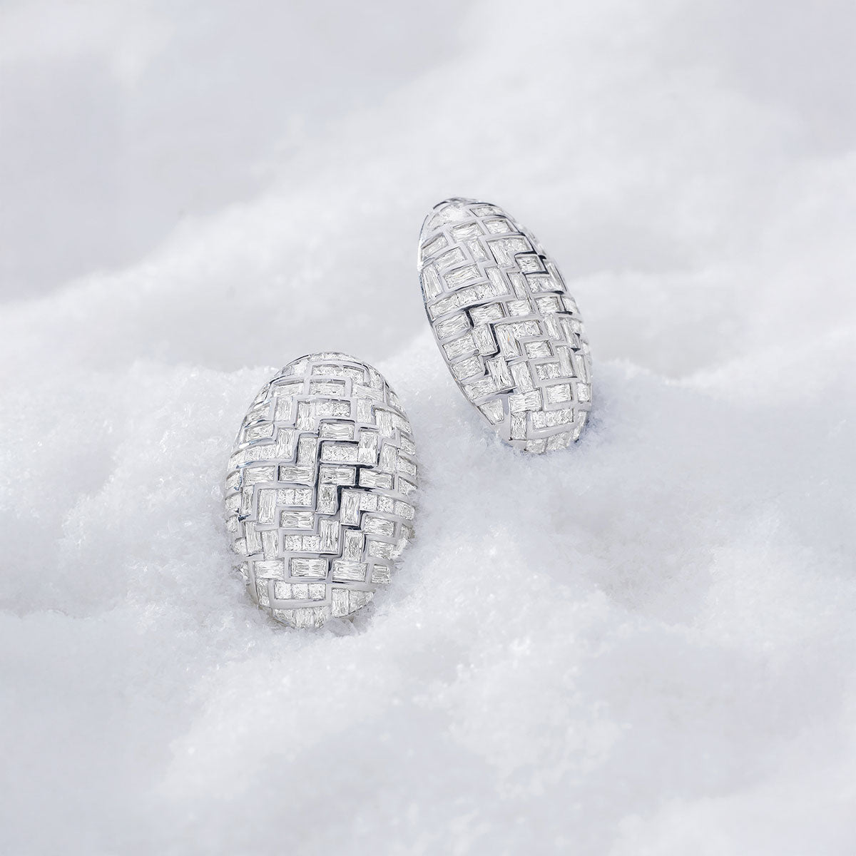 A pair of APM MONACO bold white earrings in silver on snowy surface