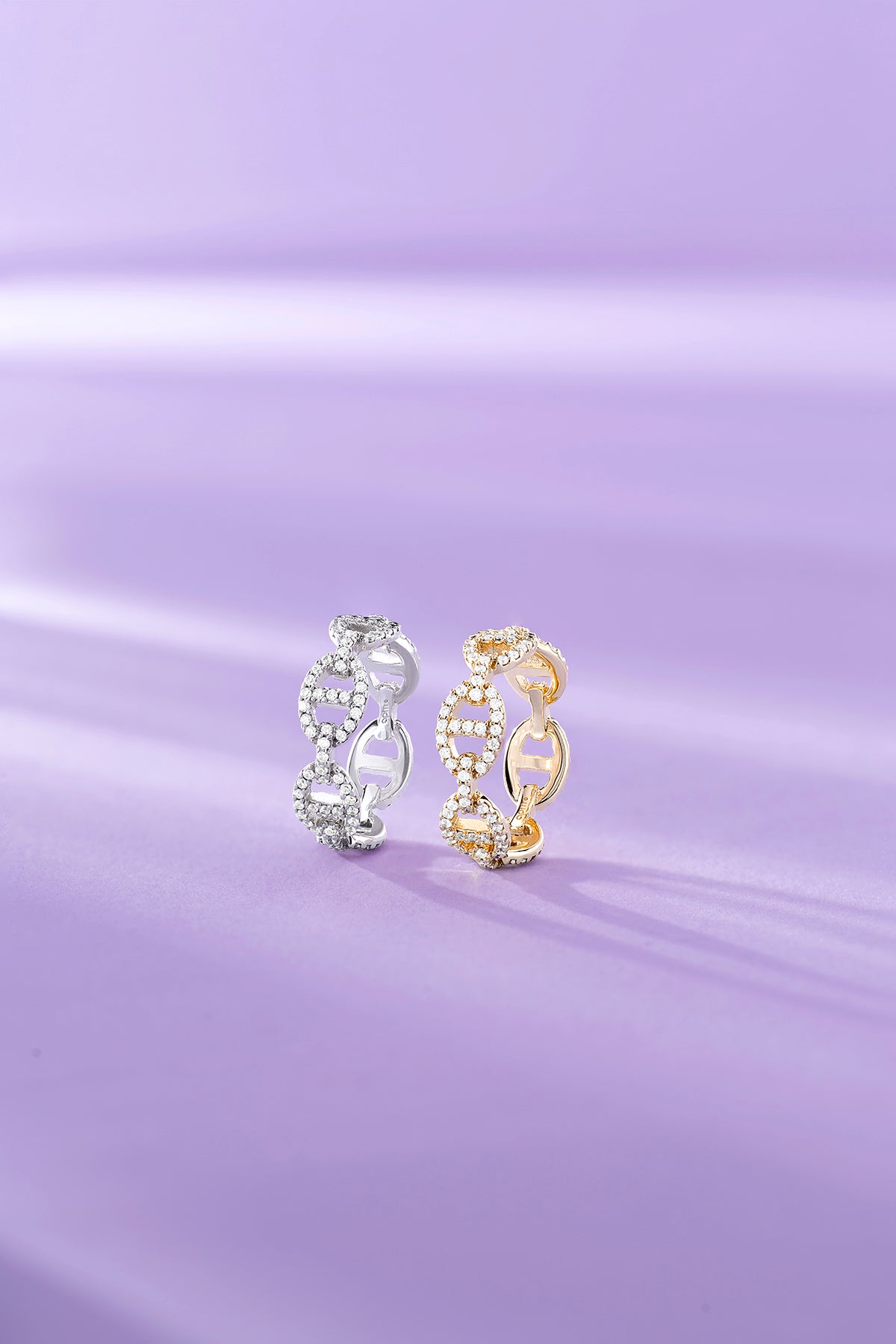 Two APM MONACO yellow gold and silver hoop earrings on a purple fabric background