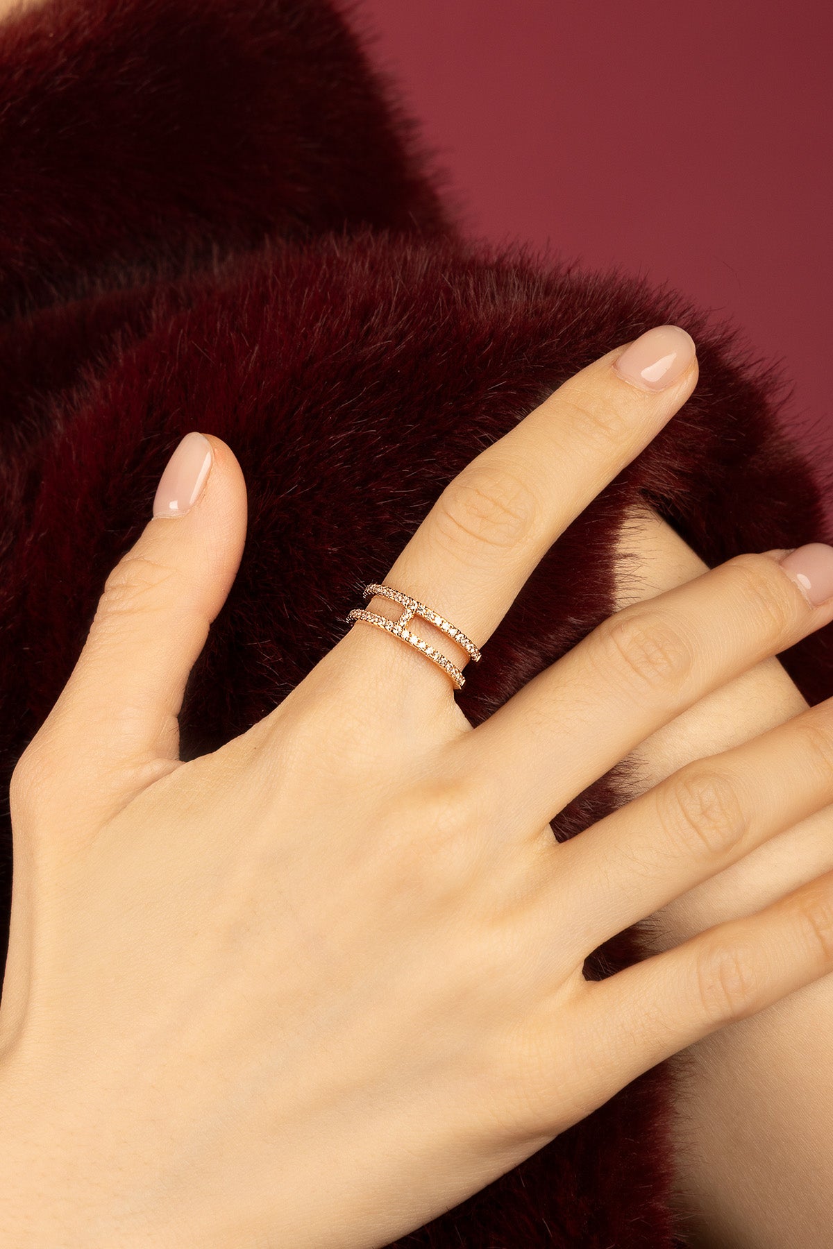 Femme portant la bague APM double ligne, éclat scintillant sur fond bordeaux.