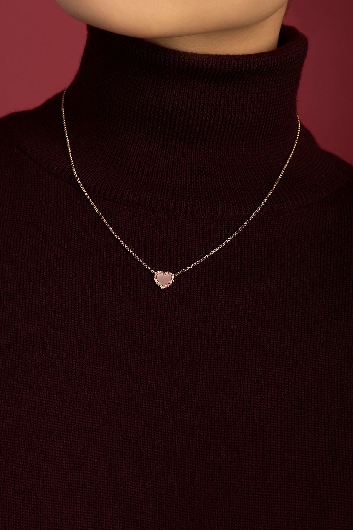 Femme portant le collier cœur APM, une touche romantique sur un col bordeaux.