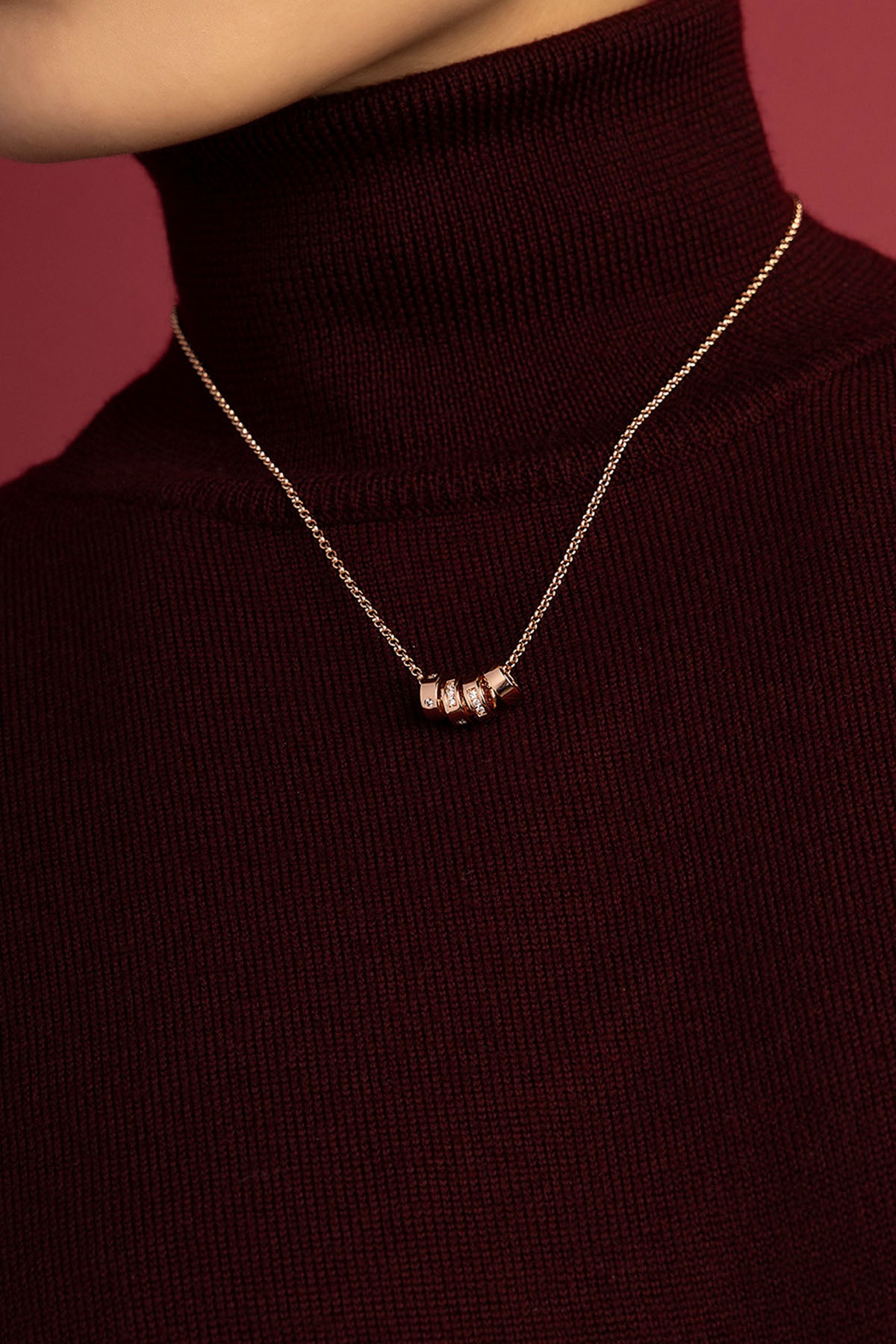 Femme portant un collier APM, délicate touche dorée sur un col bordeaux, élégance feutrée.