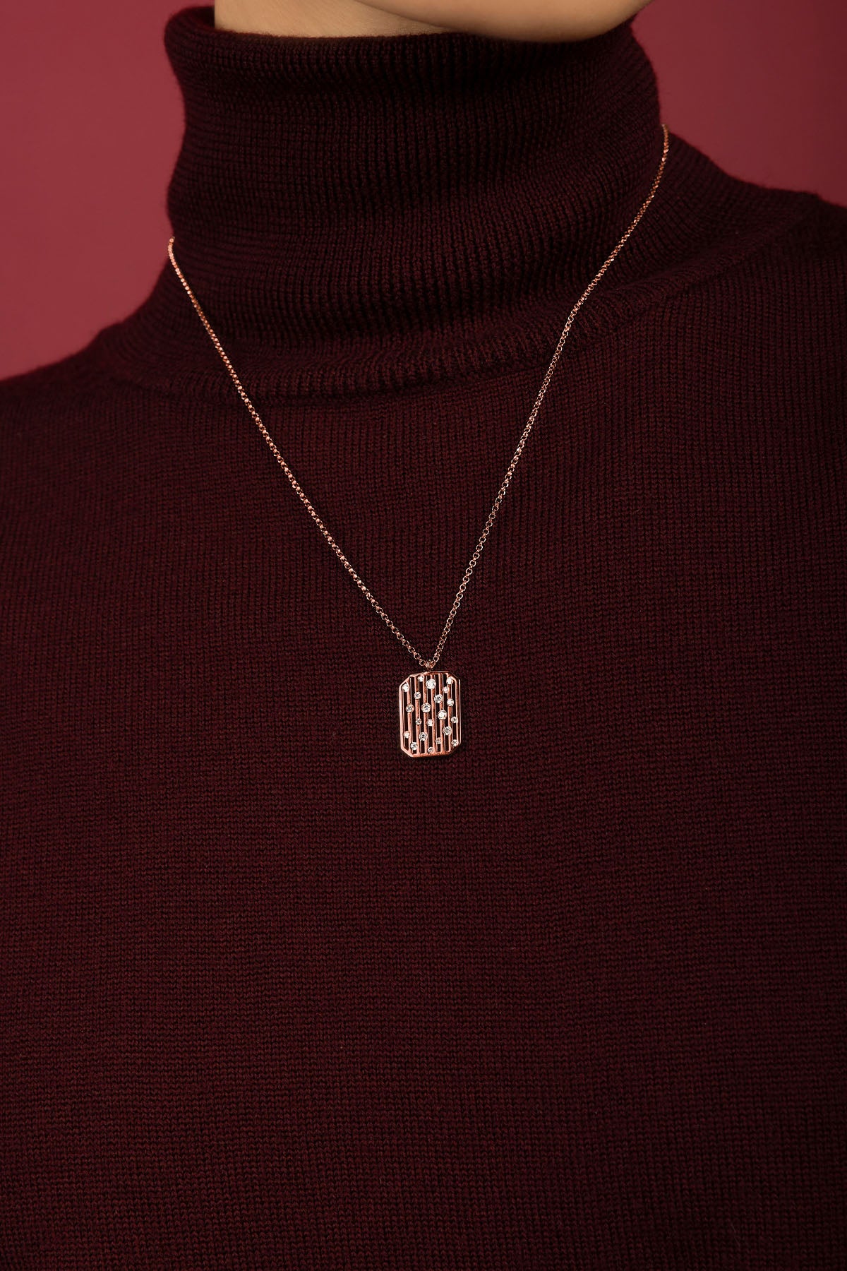 Femme portant un collier APM, éclat rosé sur col roulé bordeaux, élégance feutrée.