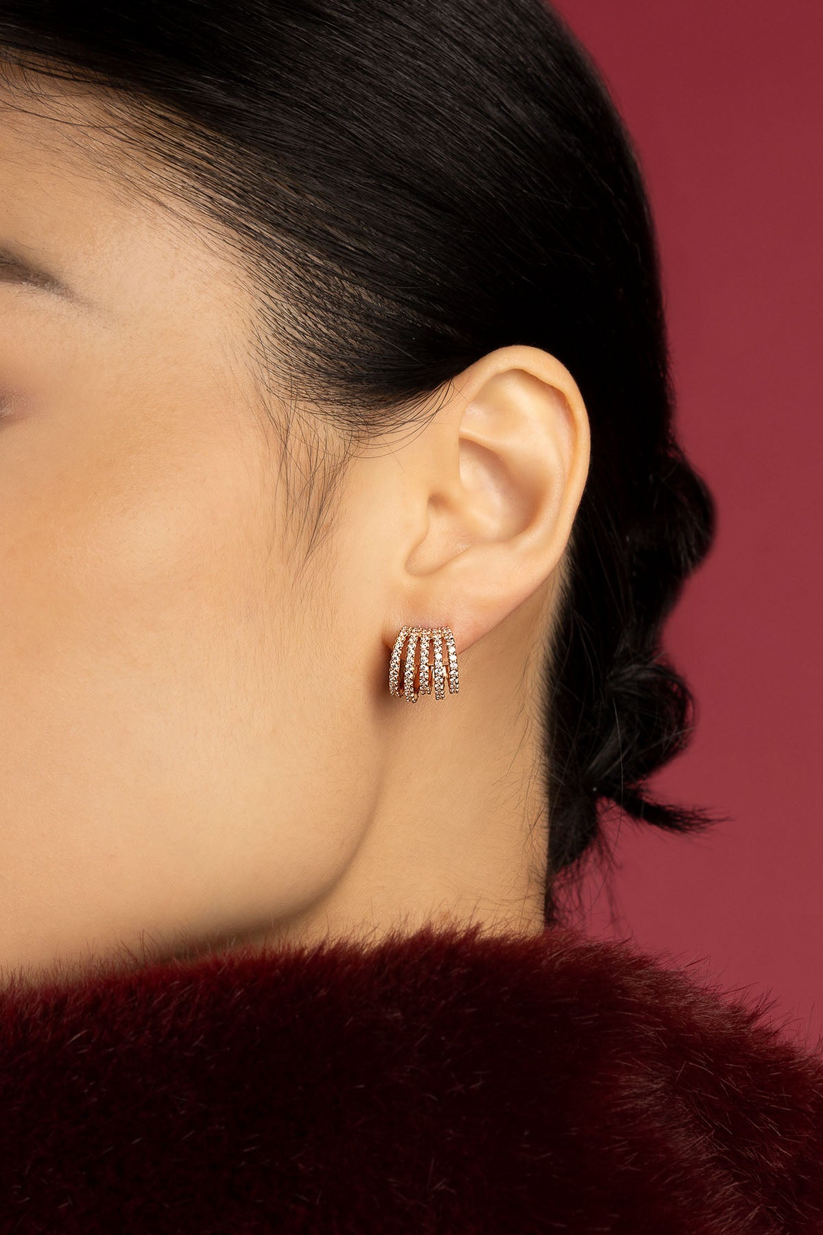 Femme portant les boucles d'oreilles APM, éclat multi-arches sur fond bordeaux envoûtant.