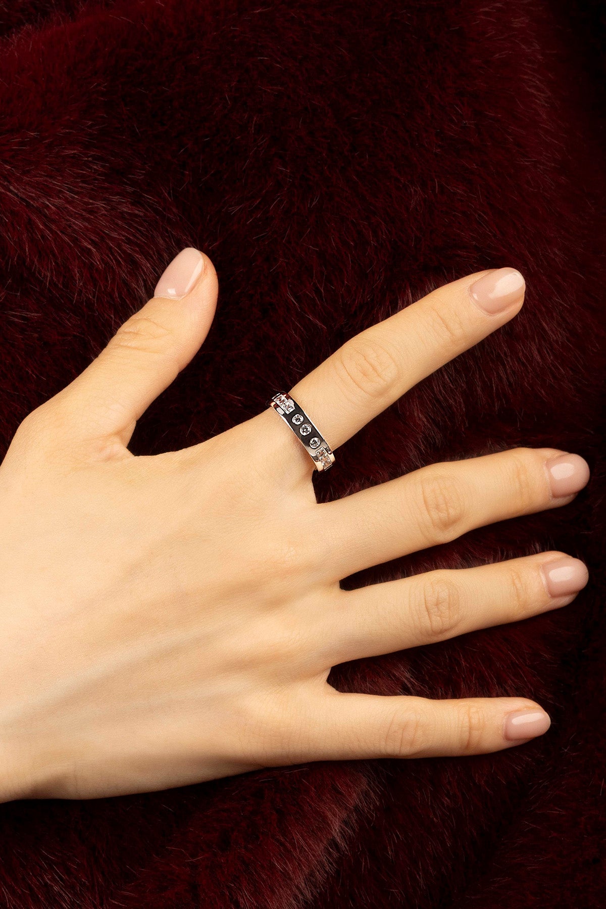 Woman wearing APM ring, éclat discret sur fourrure bordeaux, élégance intemporelle.