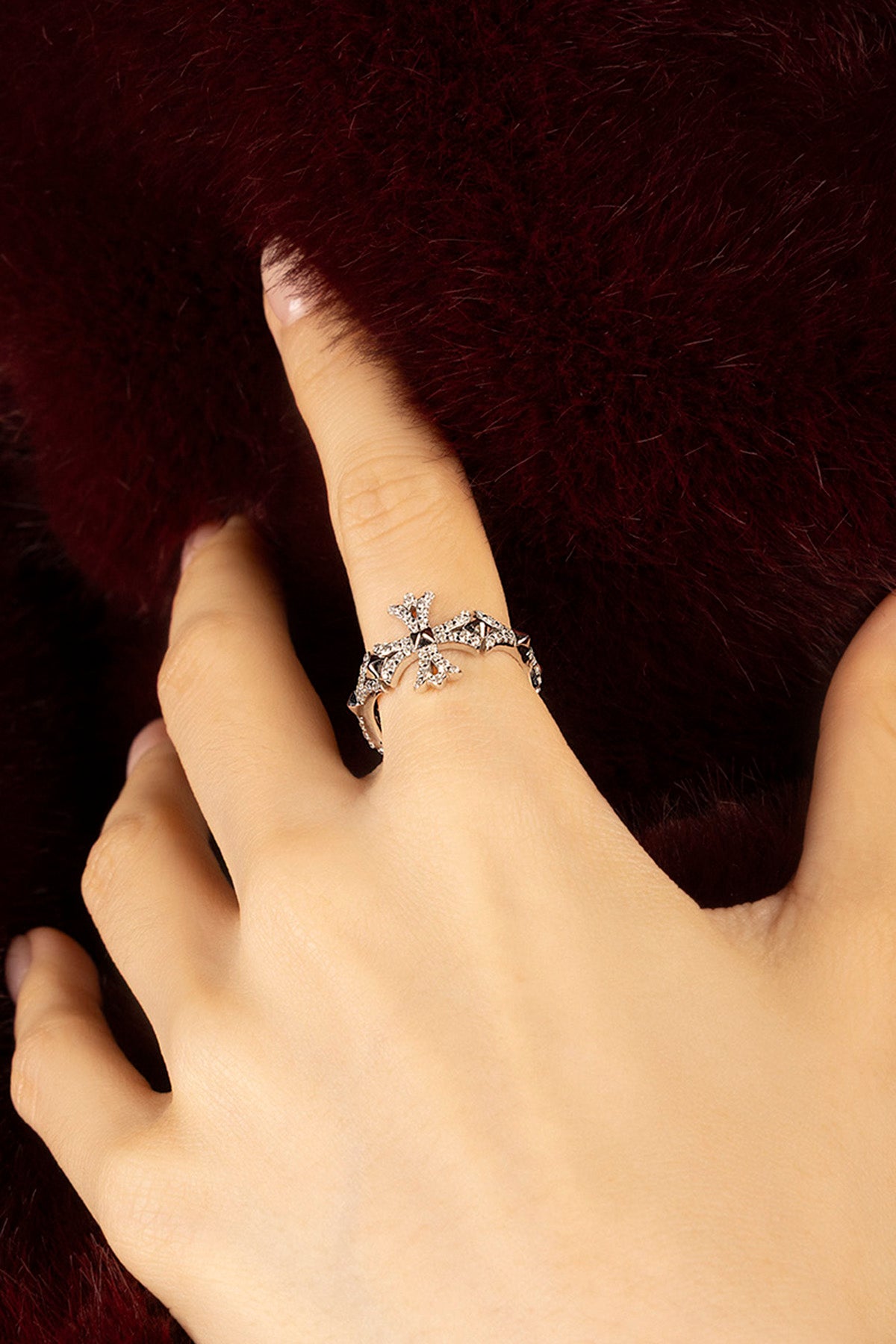 Femme portant la bague APM Monaco, une élégance scintillante sur fond bordeaux velouté.
